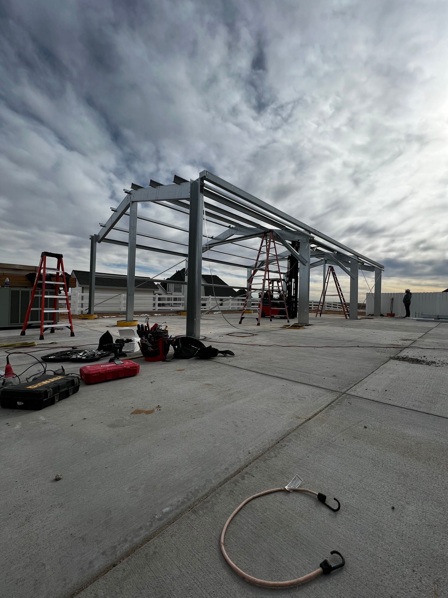 A metal framework for a structure stands on a flat concrete rooftop under a cloudy sky, with tools scattered around.