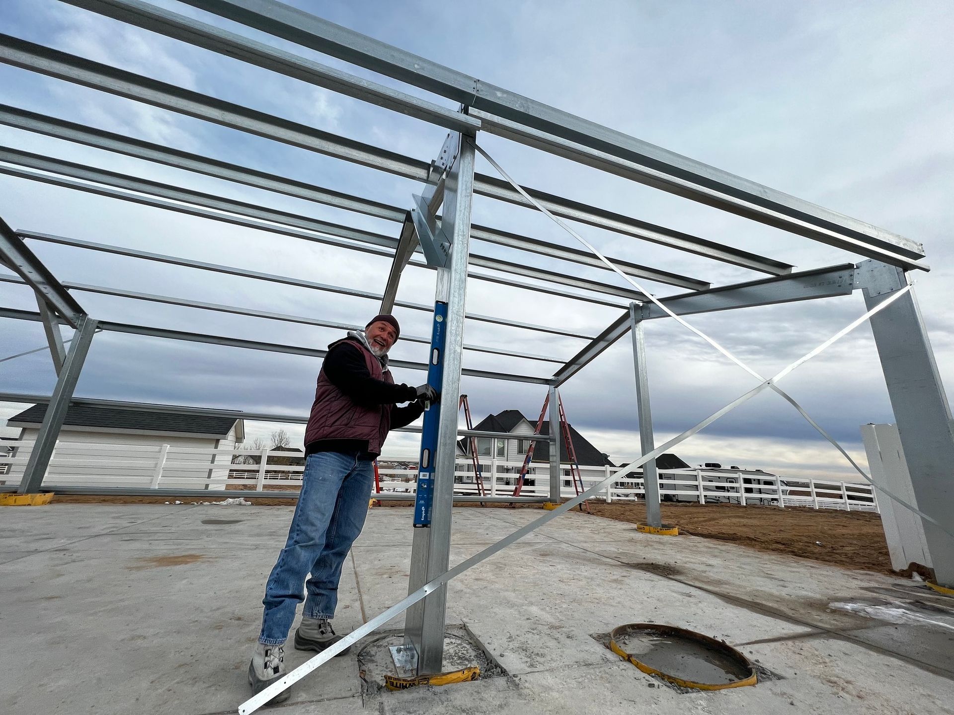 A person uses a level to adjust a steel support beam on an outdoor construction site with a partially built frame.