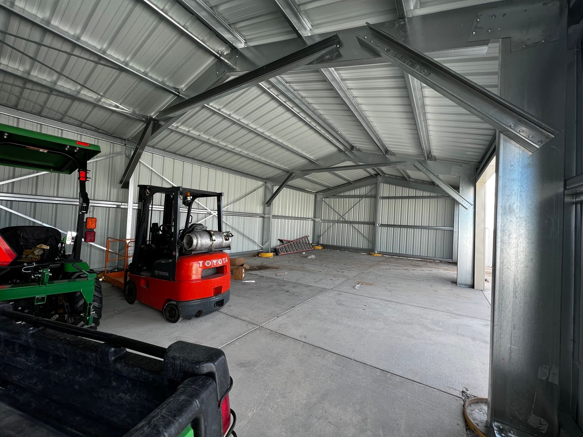 A wide-angle view of a metal barn interior featuring a red forklift and green agricultural equipment on a concrete floor.