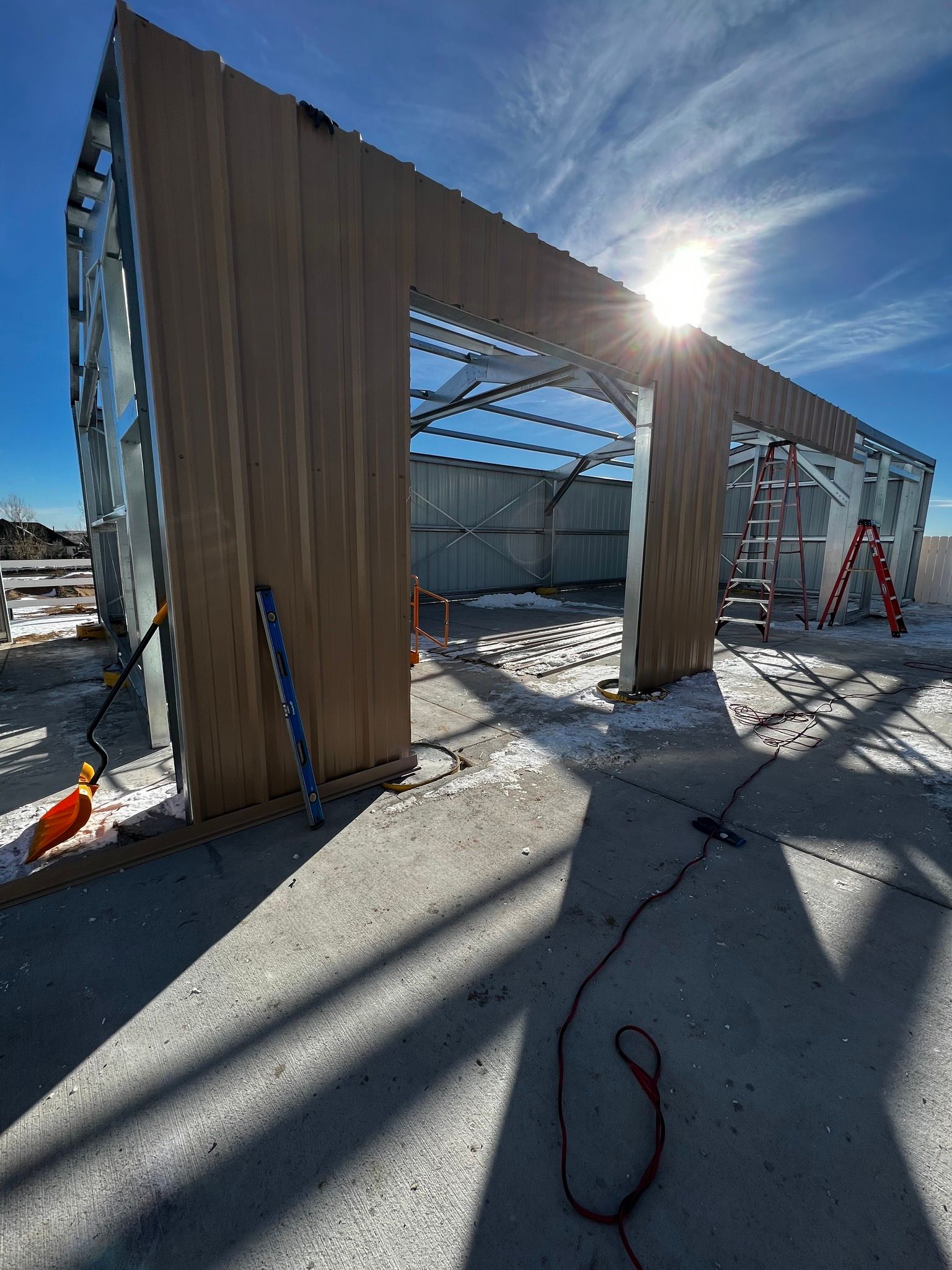 The metal frame of a building under construction, featuring vertical wood-look siding panels under a bright, sunny sky.