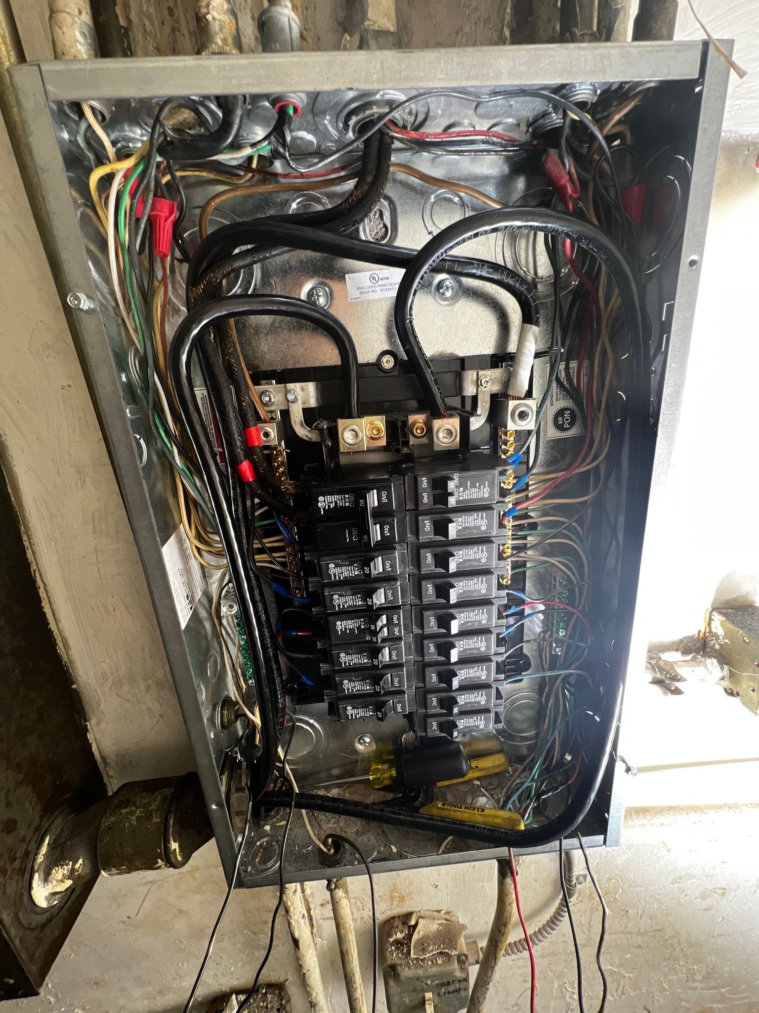 An open electrical breaker panel with multiple black circuit breakers and thick black wiring in a metal box.