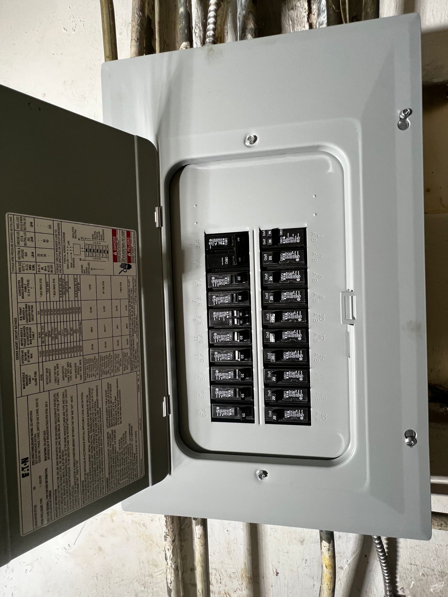 An open gray residential electrical breaker box mounted on a wall with multiple circuit breakers visible inside.