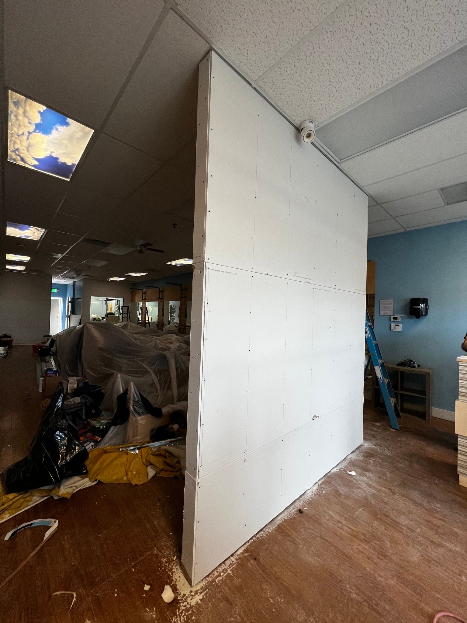 A newly installed white drywall partition wall stands in an office space under renovation.
