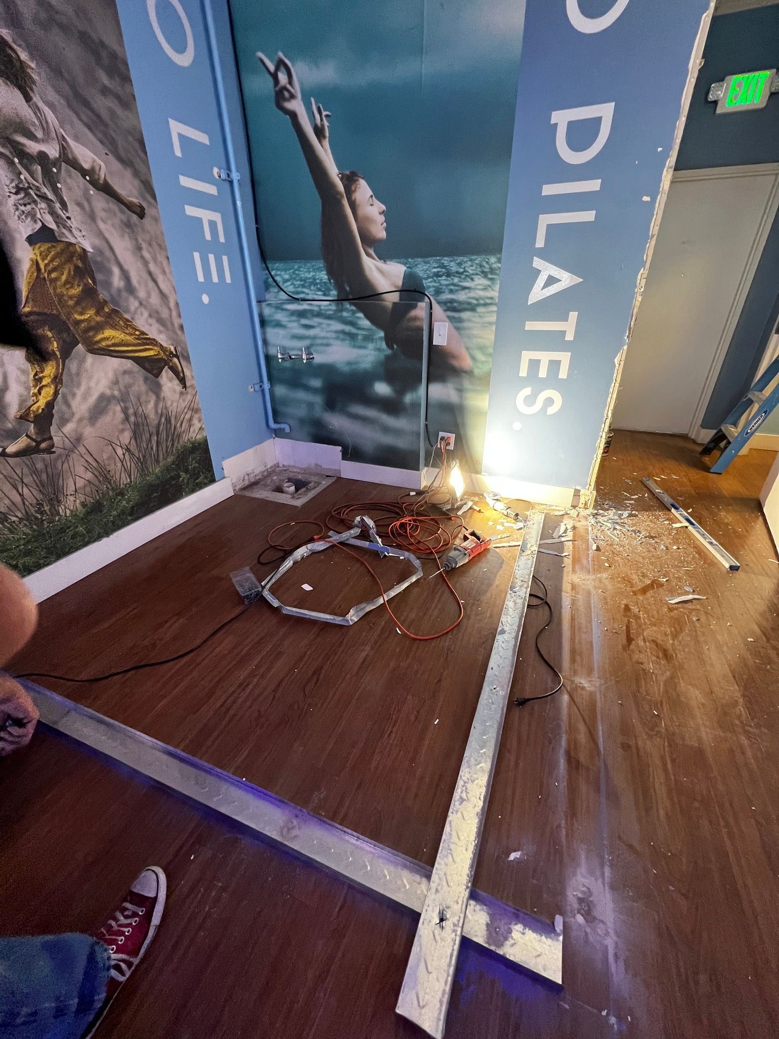 A room under construction with a Pilates wall mural, loose electrical wiring, and metal floor framing on wood flooring.