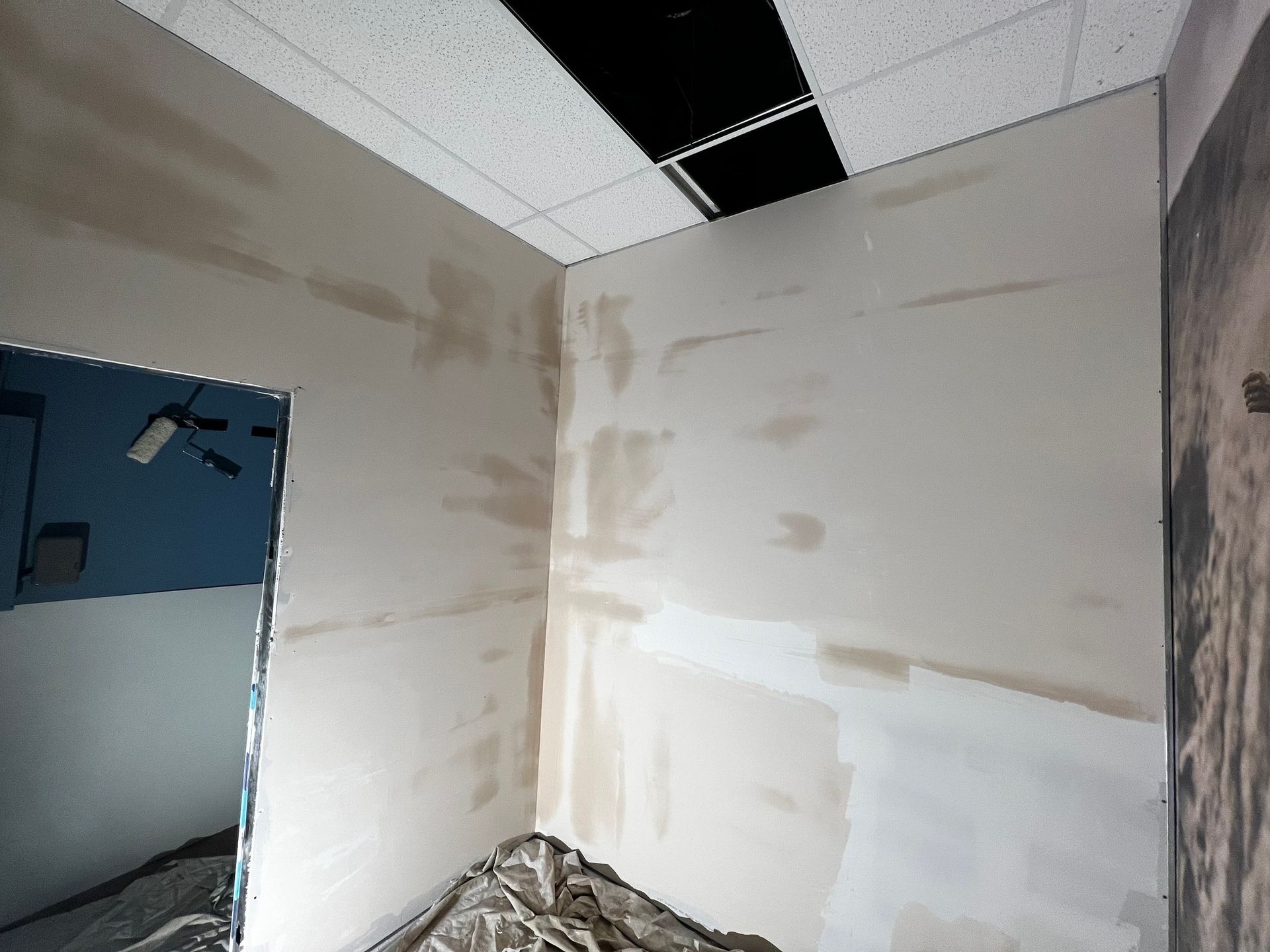 A room under construction with unpainted drywall, patchy joint compound, and a missing ceiling tile.