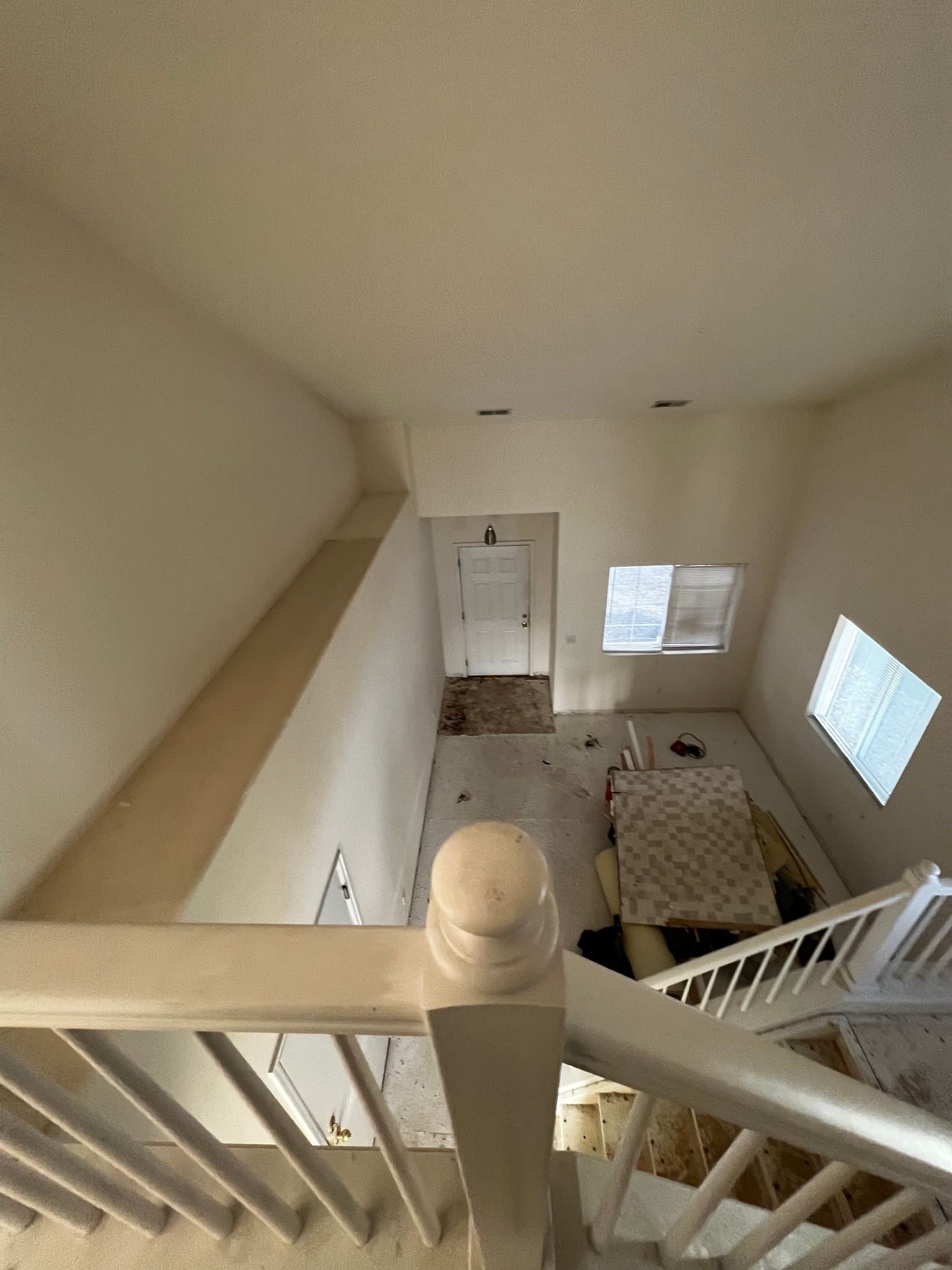 A high-angle view looking down from a carpeted staircase into a sparsely furnished, neutral-toned living room.