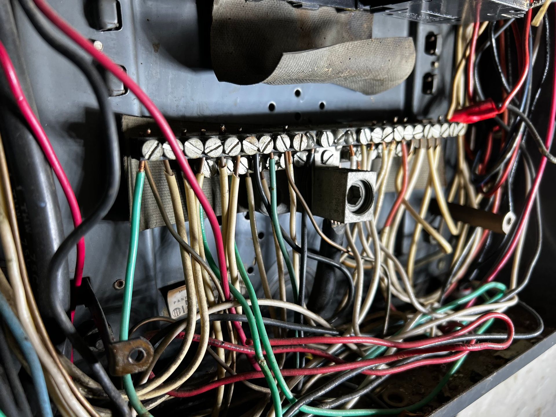 A mess of white, black, red, and green electrical wires connected to a metal terminal block inside a breaker panel.
