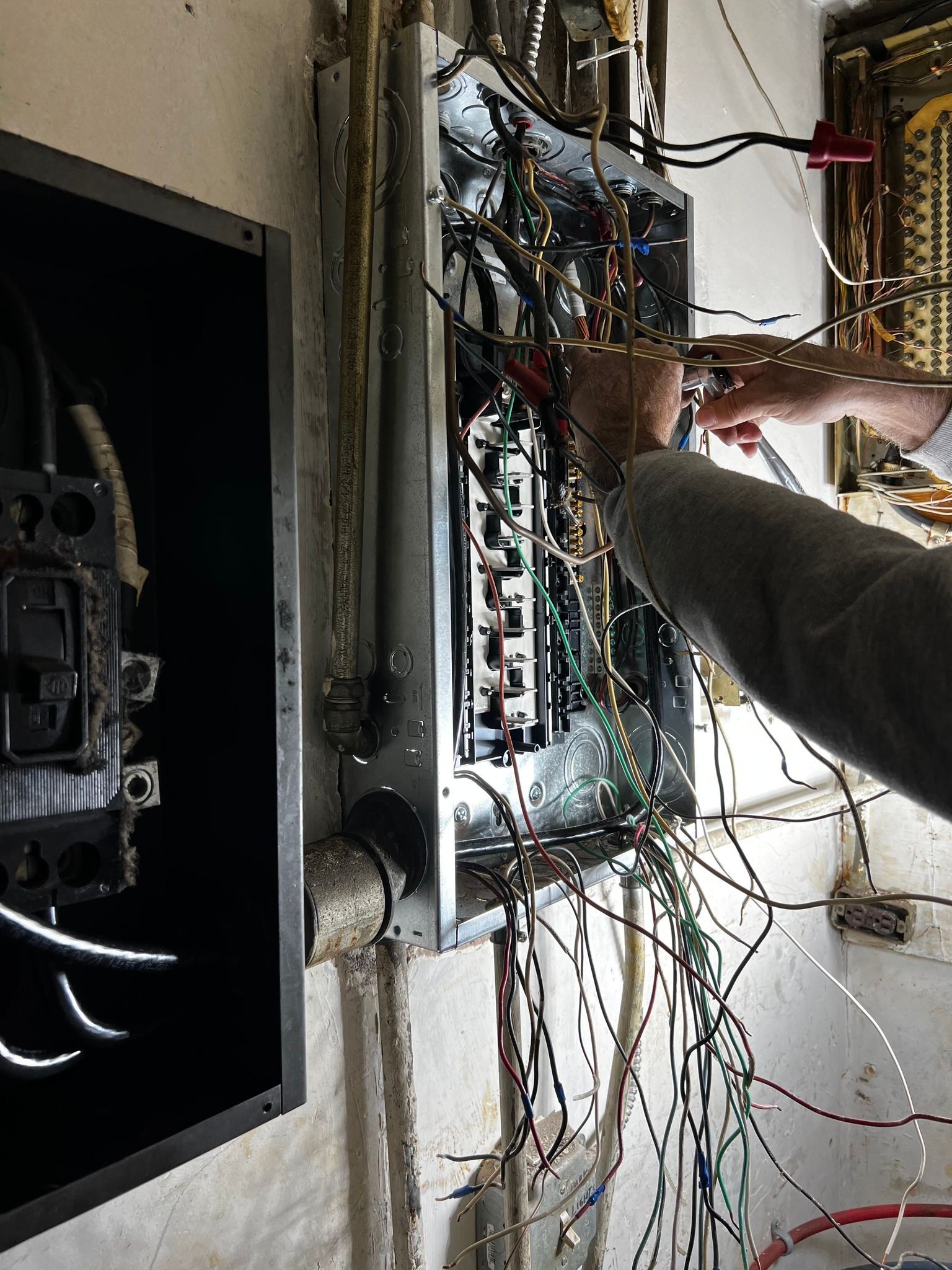 A person working on the wiring inside an open electrical breaker panel mounted on a wall.