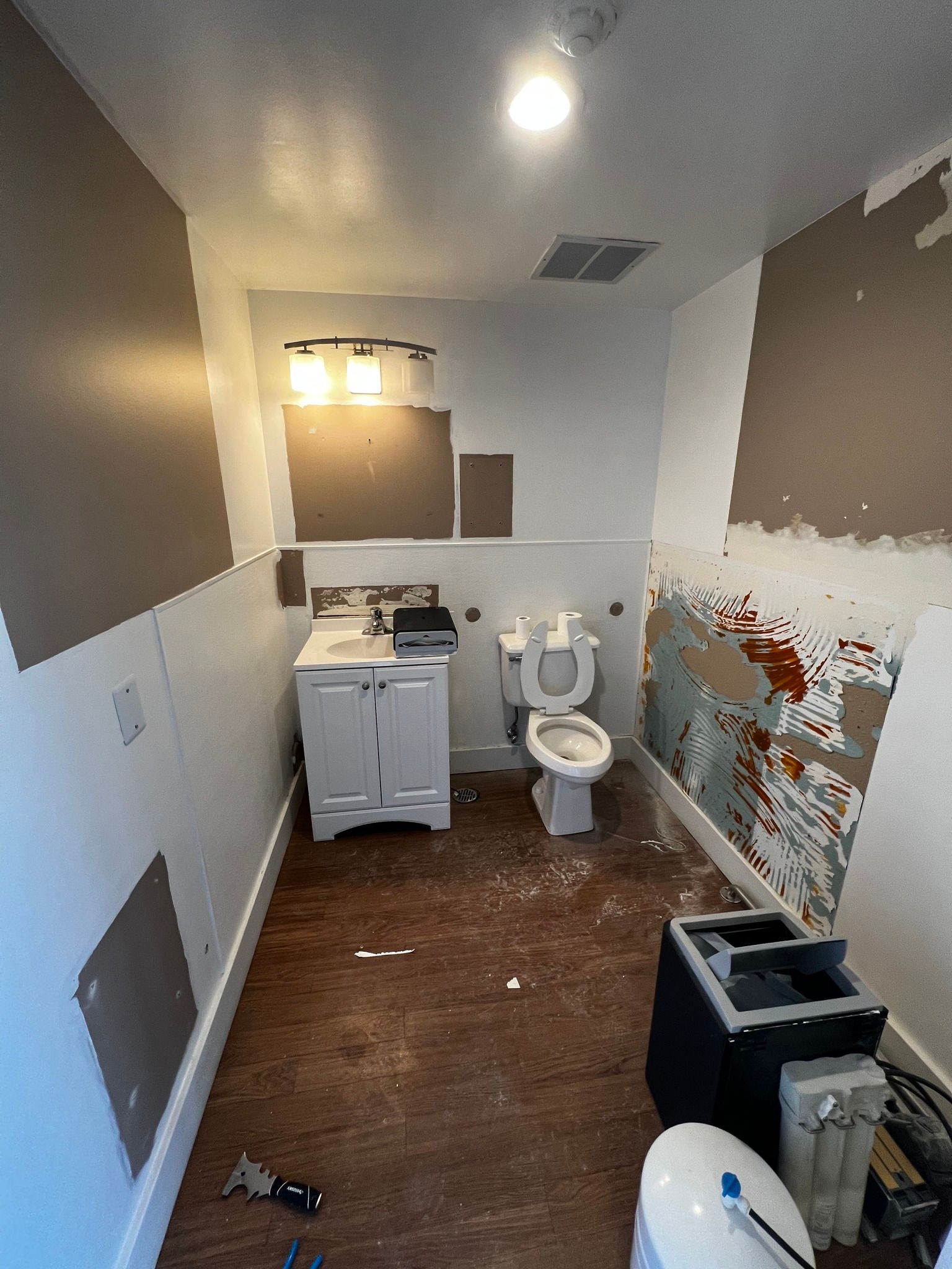 A bathroom under renovation with exposed wall patches, a vanity, a toilet, and debris on the floor.