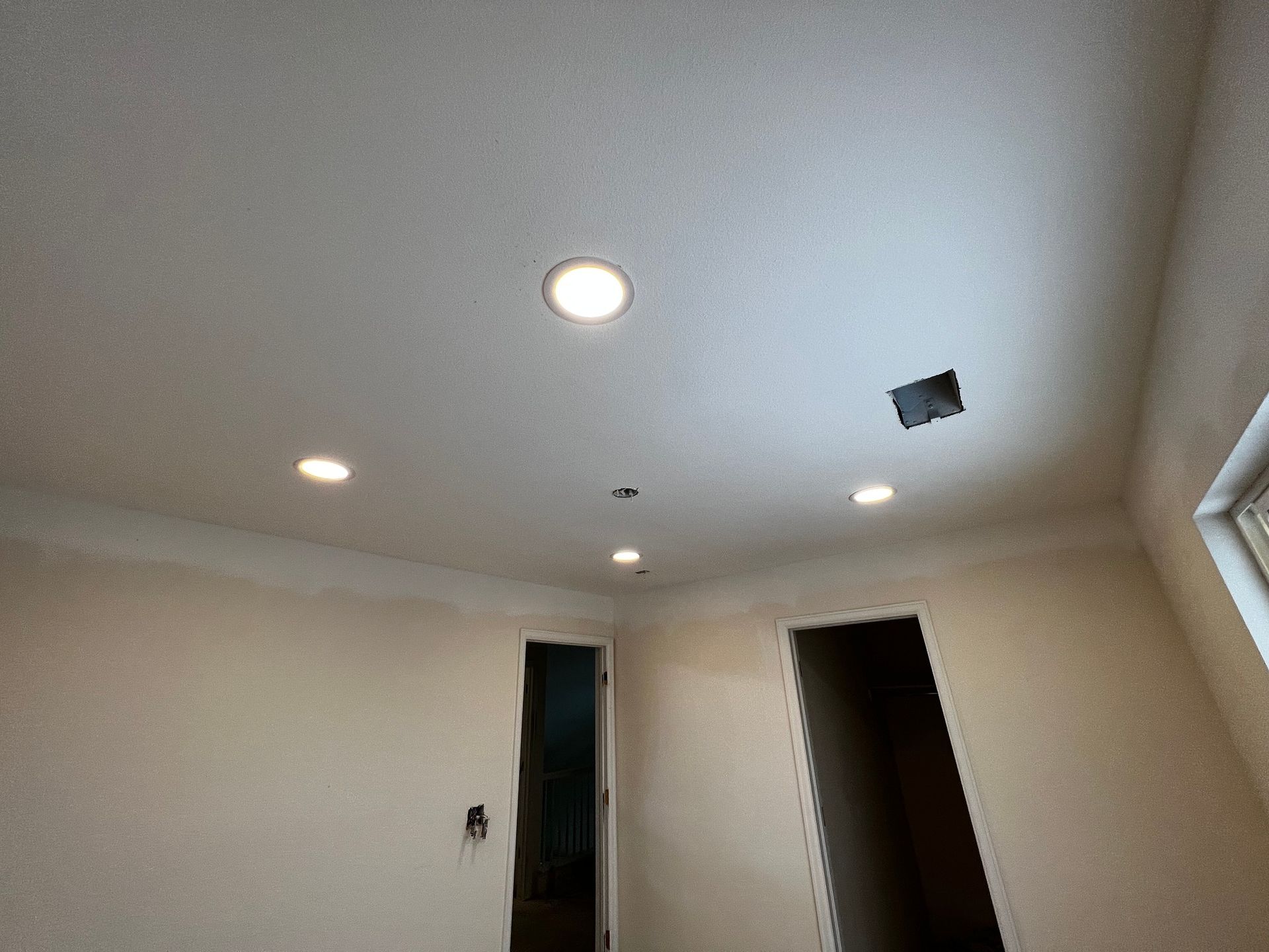 A room interior featuring a ceiling with four recessed lights, a small open electrical box, and two doorways.
