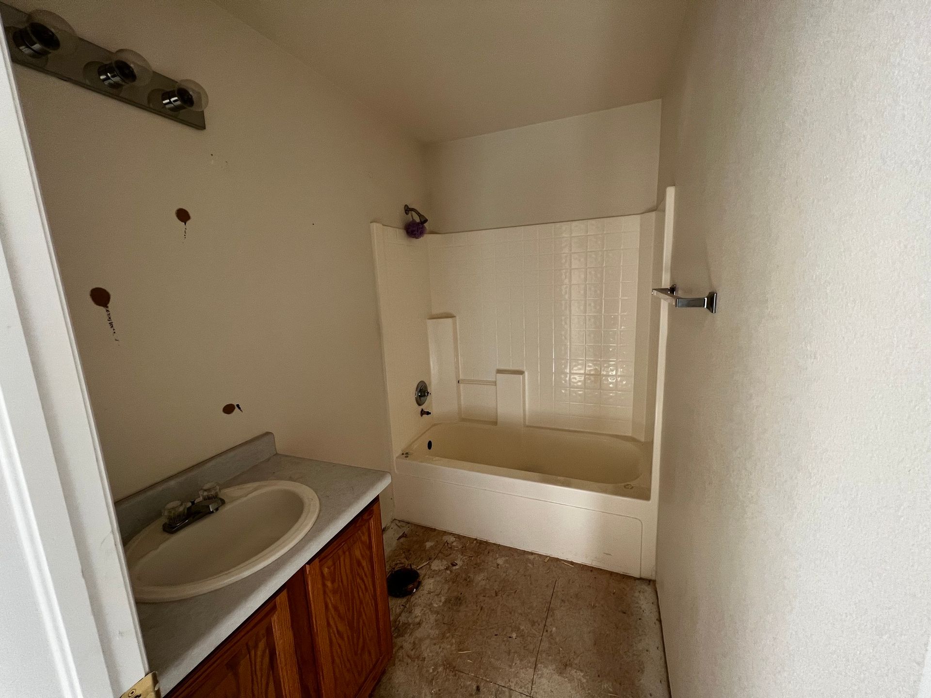 A dimly lit bathroom with a vanity sink, wooden cabinet, and a white bathtub-shower combo in need of renovation.