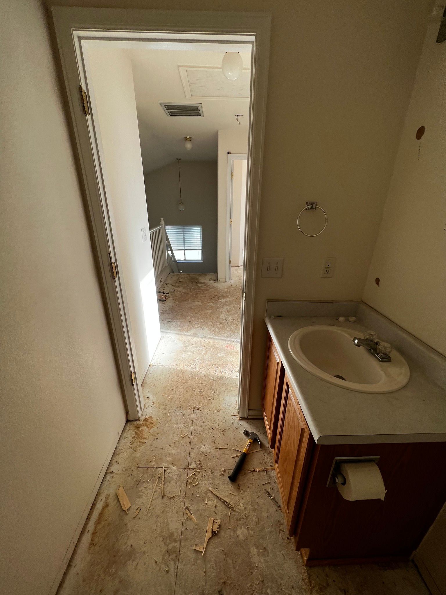 A bathroom undergoing renovation with debris on the floor, a vanity sink, and an open doorway leading to a hallway.