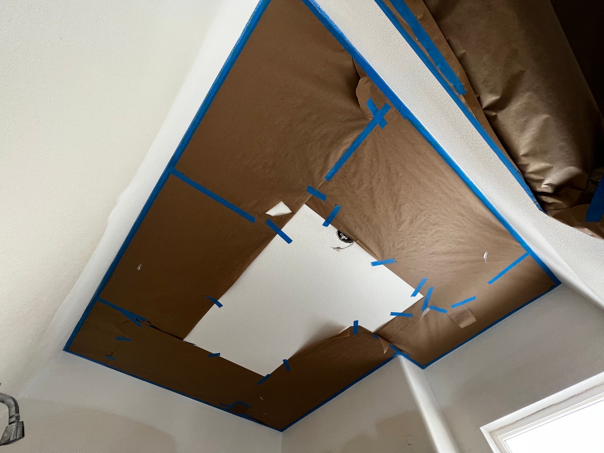A ceiling area prepared for painting, with protective brown paper taped around a white patch of drywall.