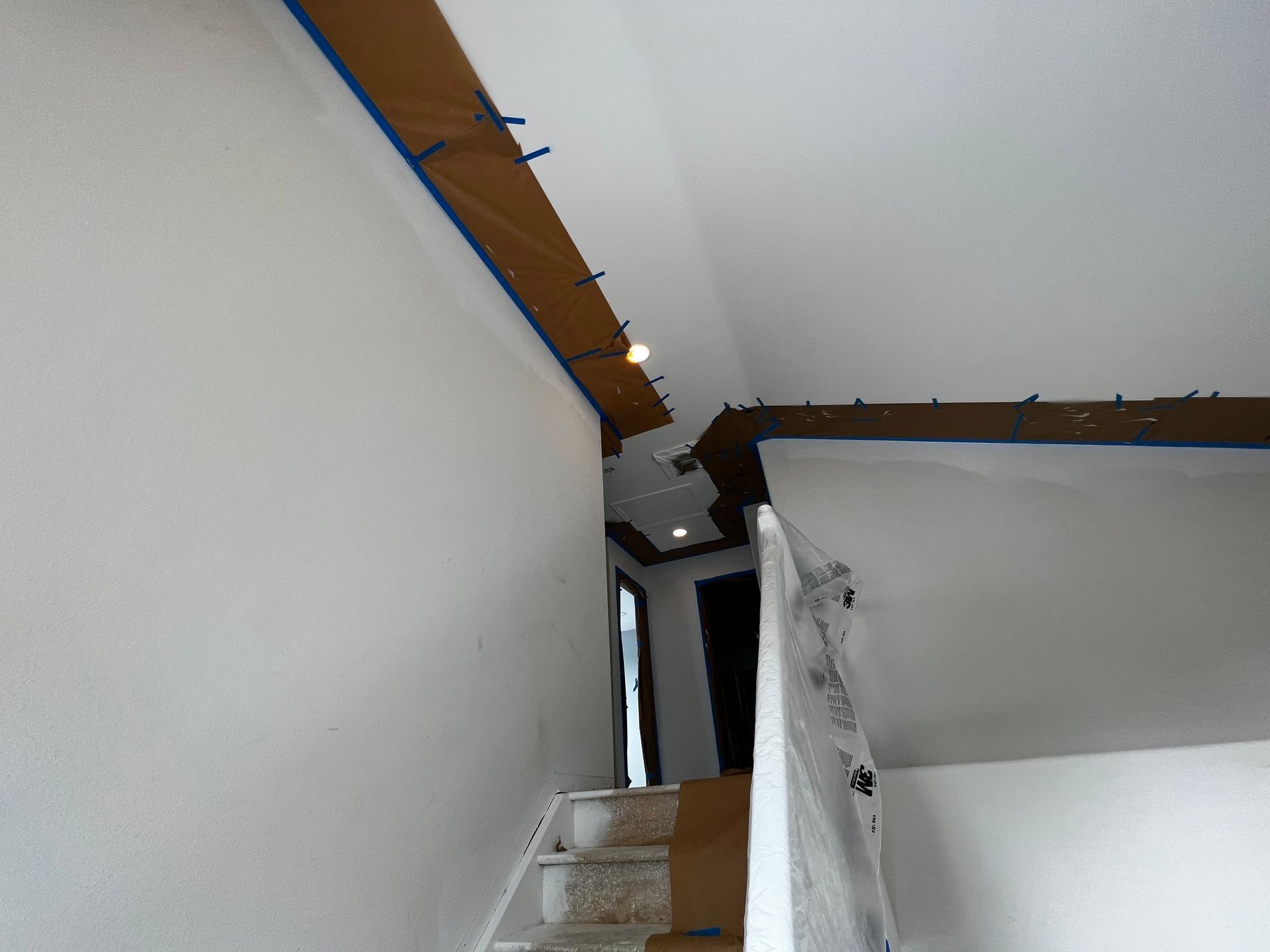 A staircase interior under construction with taped-off sections and protected railings for painting.