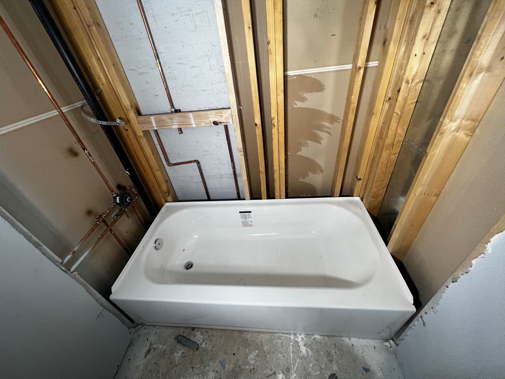 A white bathtub installed in a bathroom under construction, featuring exposed wooden studs and wall plumbing.