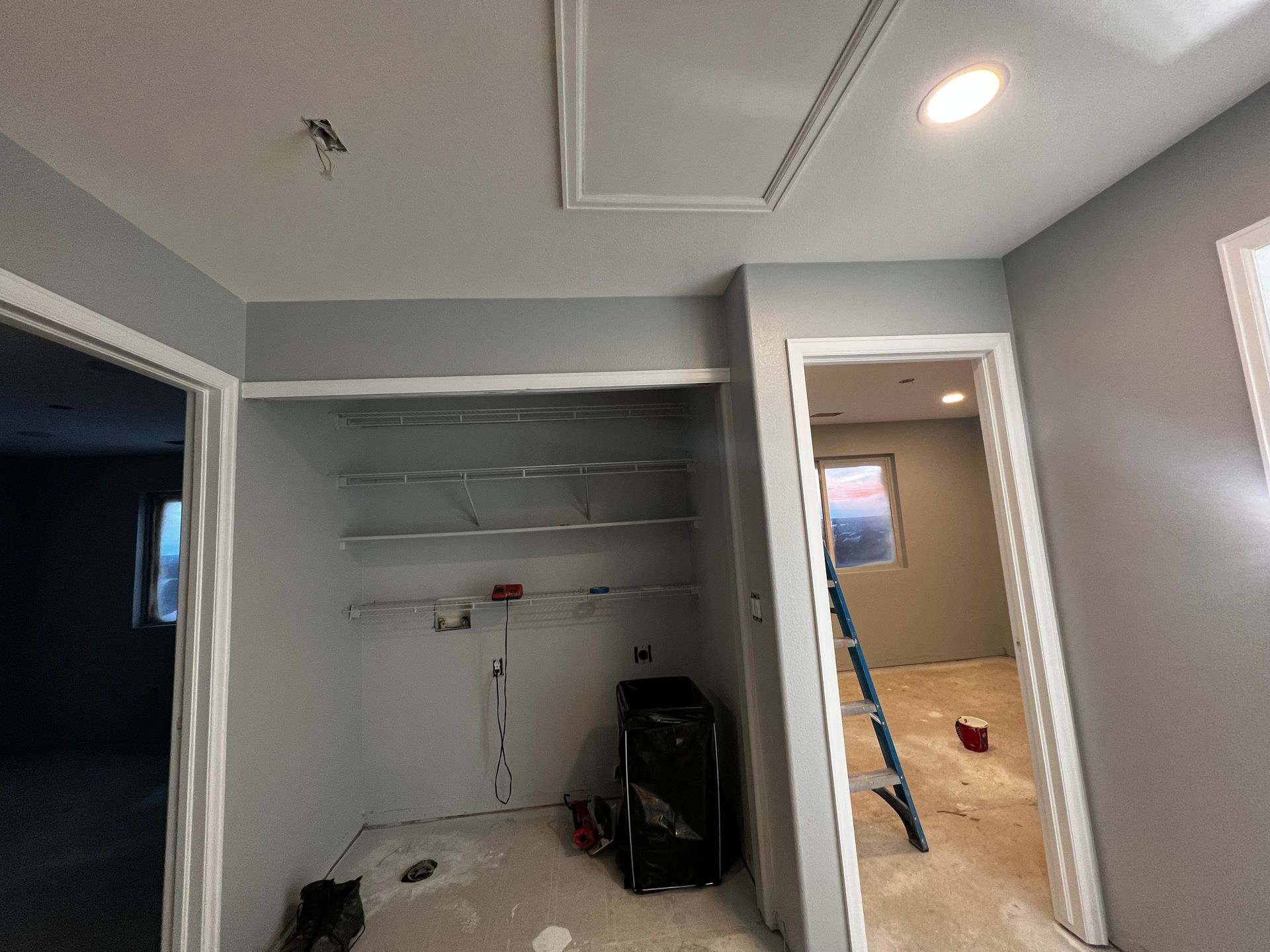 A room under renovation with gray walls, an open closet with wire shelving, a doorway leading to a ladder, and ceiling light.