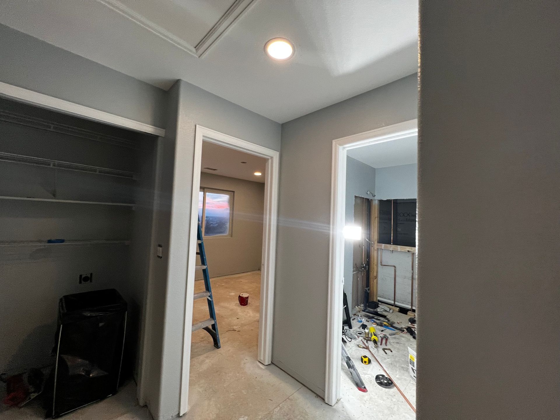 An interior view of a hallway under construction with gray walls, two open doorways, and debris on the unfinished floor.