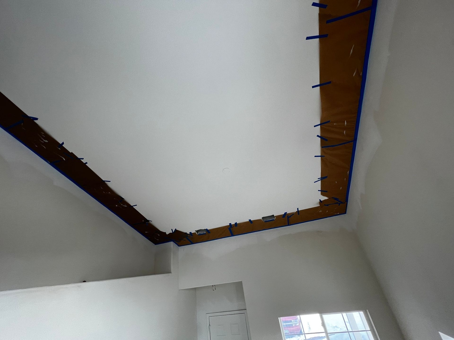 A ceiling under renovation featuring a central painted white area bordered by dark, taped-off wooden trim.