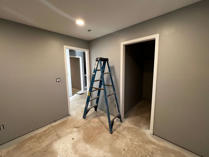 A room with gray walls and a stepladder in the center, flanked by two doorways, with an unfinished floor.