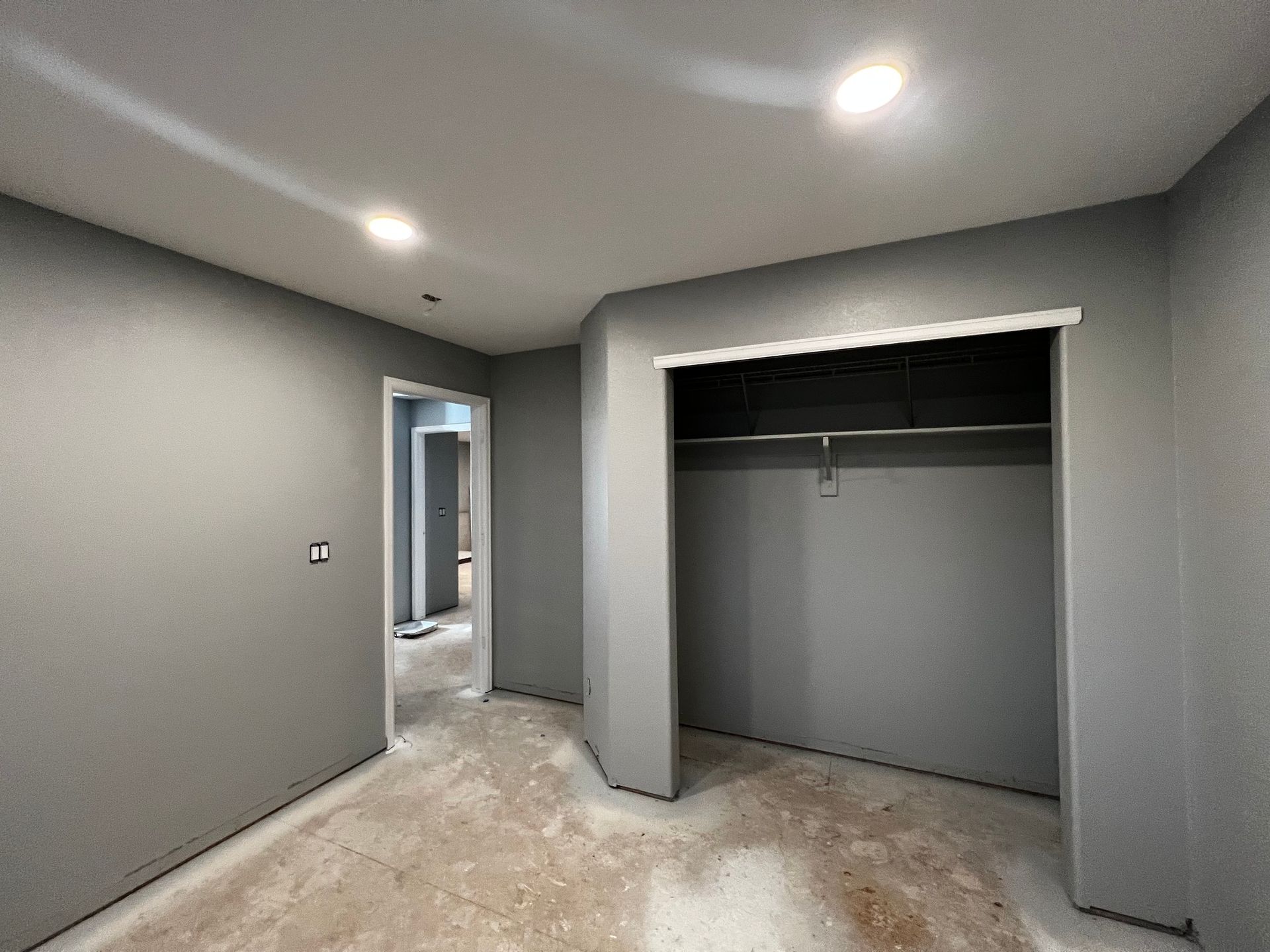 A room under renovation with grey walls, an open closet, and unfinished flooring.