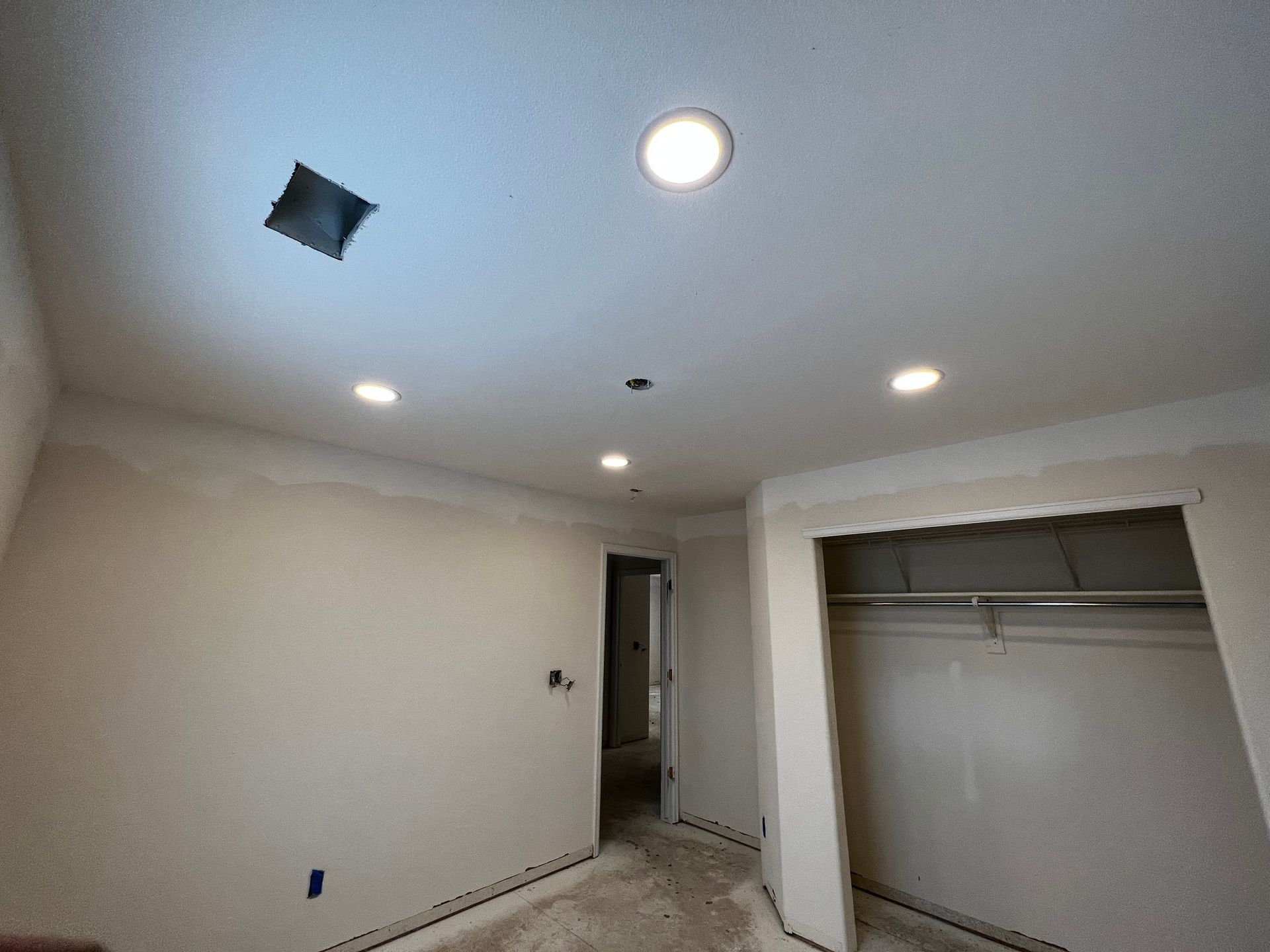 A room under renovation with beige walls, newly installed recessed ceiling lights, and an open closet.