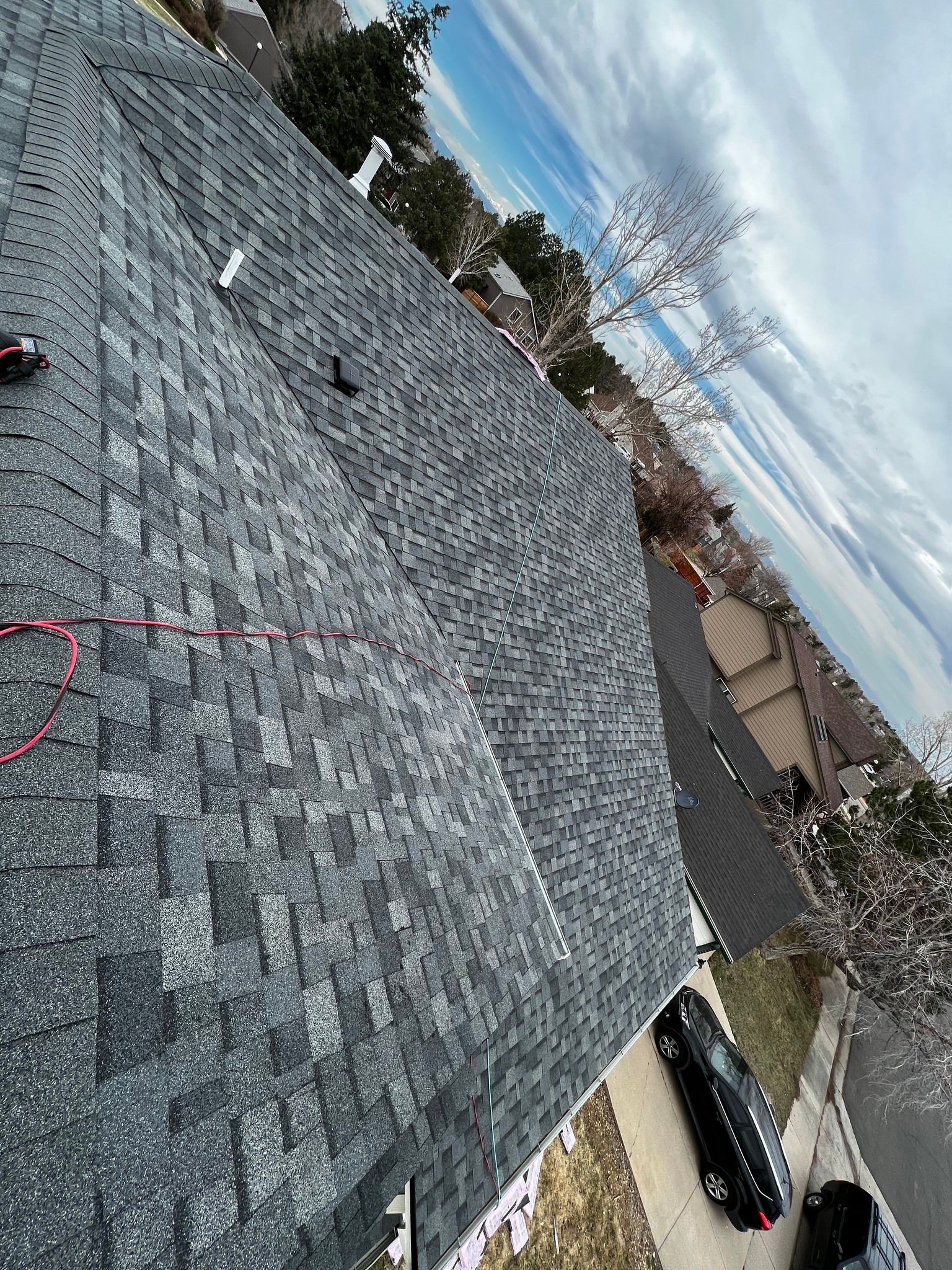 A high-angle view of a grey shingled roof under a cloudy sky, showing a residential neighborhood and street below.