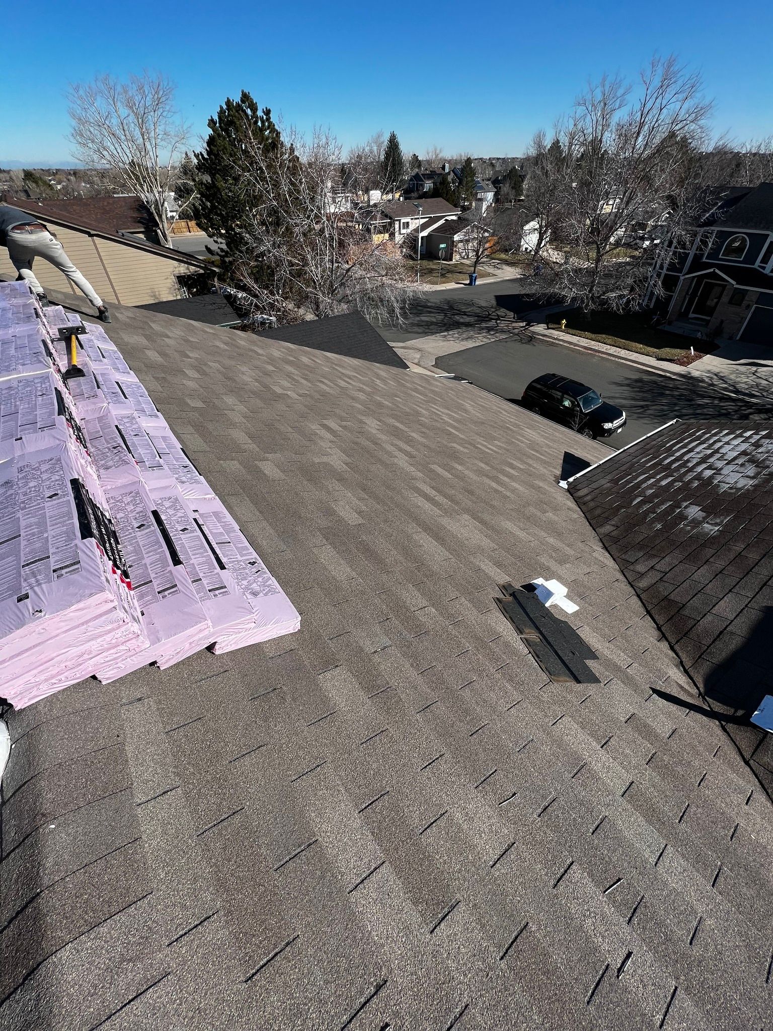 A high-angle view of a residential roof under repair, showing shingles and a stack of purple insulation panels.