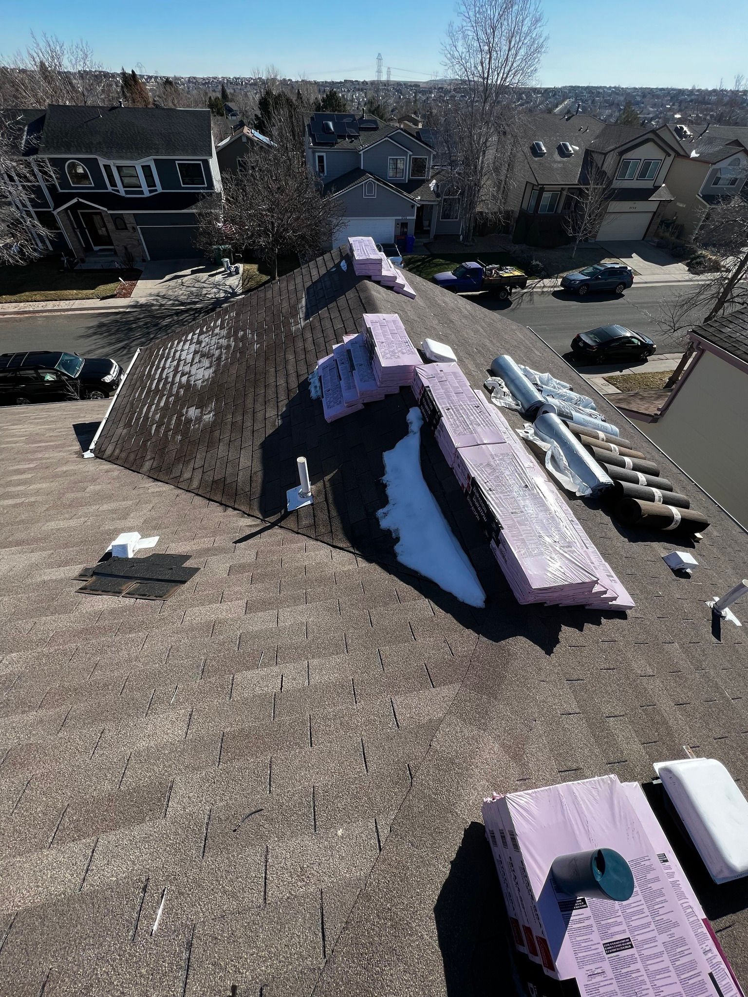 A high-angle view of a residential roof under repair, featuring scattered purple insulation boards and dark shingles.