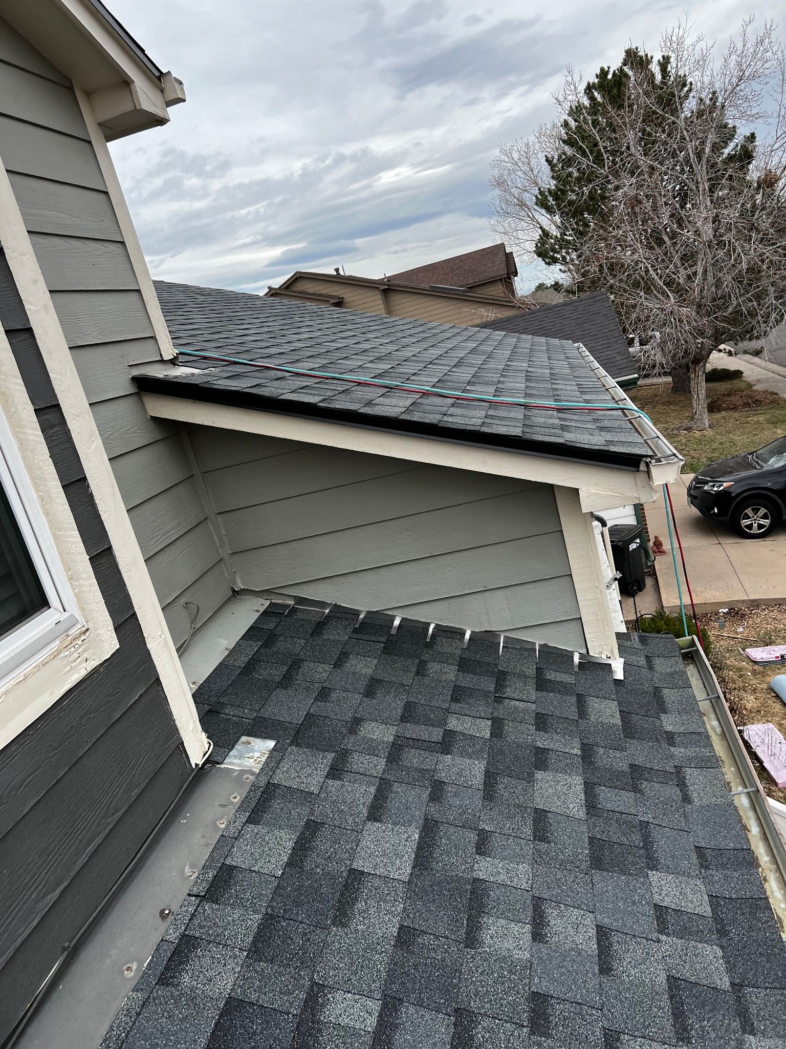 A view of a roof with dark gray shingles transitioning into a lower, flatter section, attached to a light gray house.