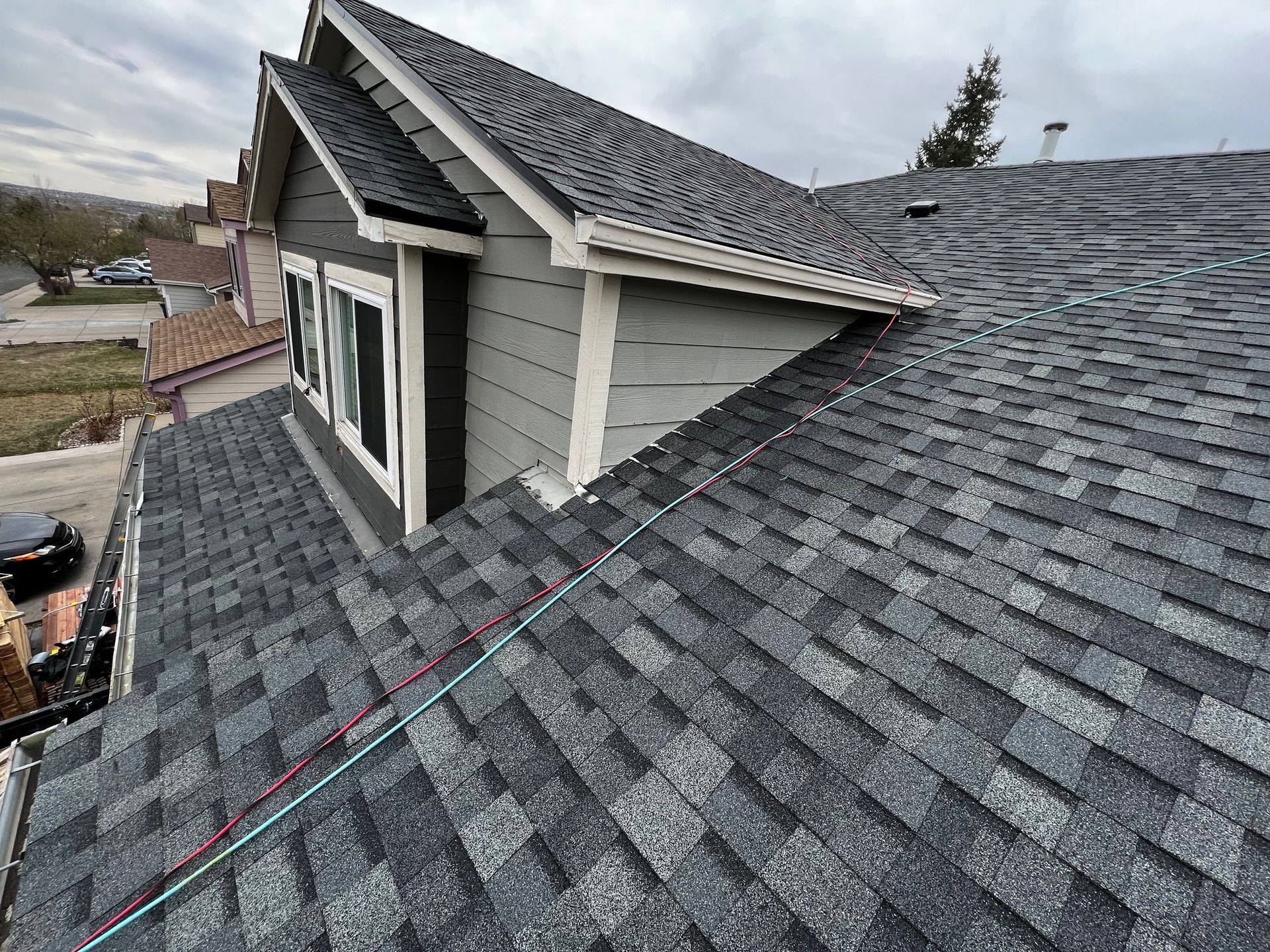 High-angle view of a residential shingled roof with a dormer window, seen on an overcast day.