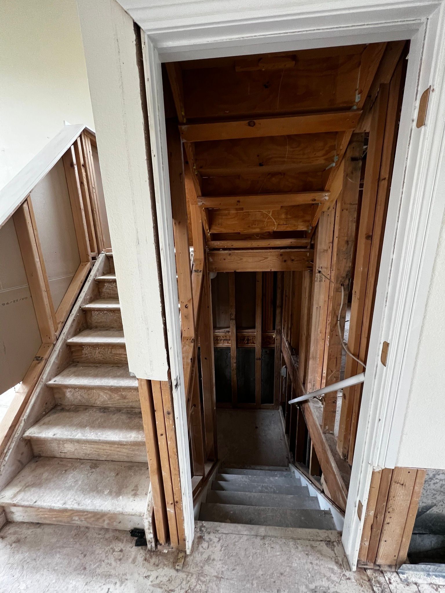 Construction scene showing two open staircases under renovation, with exposed wooden framing and partial drywall.