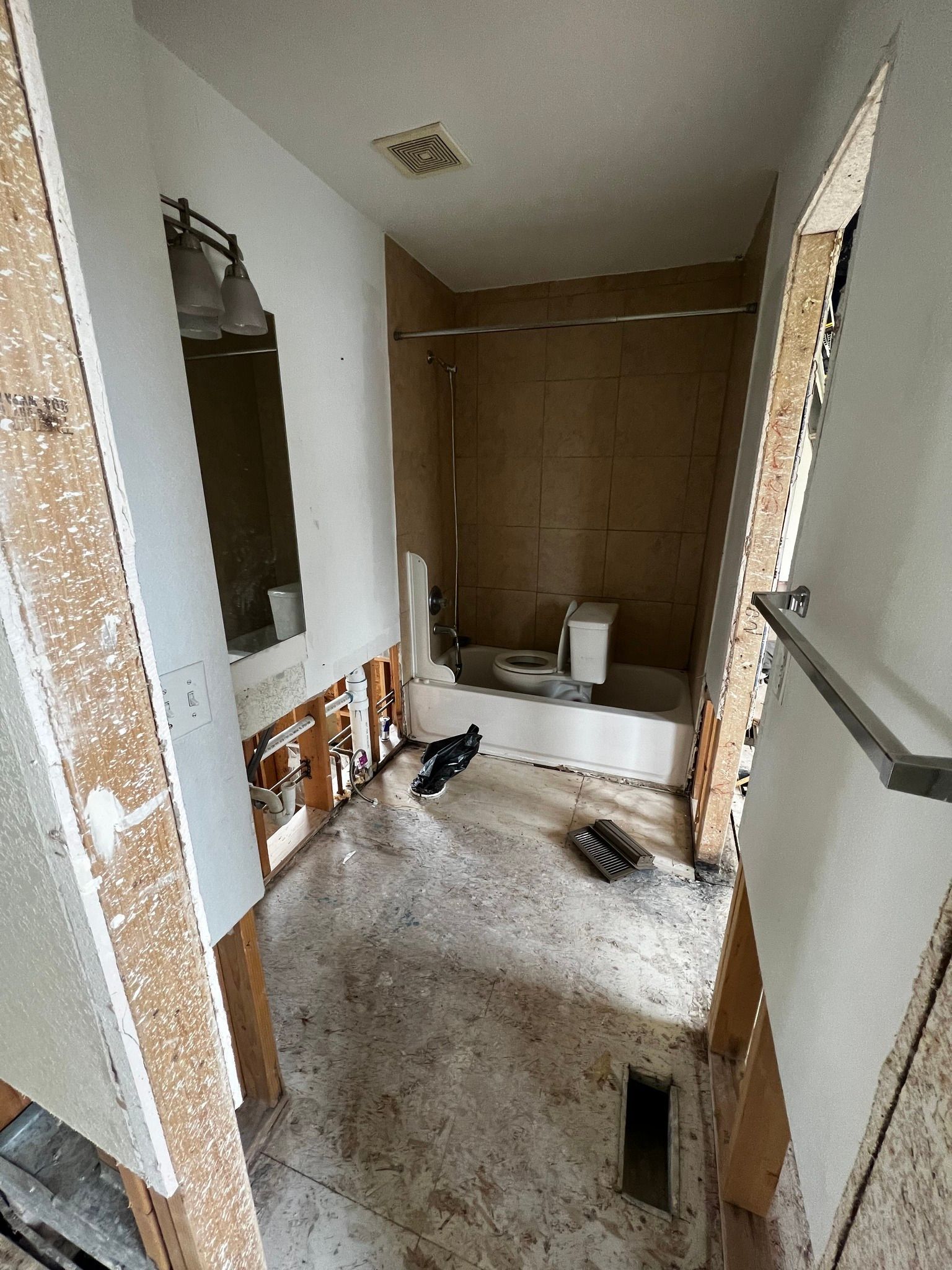 A bathroom undergoing renovation, showing exposed wall studs, a partially demolished vanity, and a bare bathtub area.