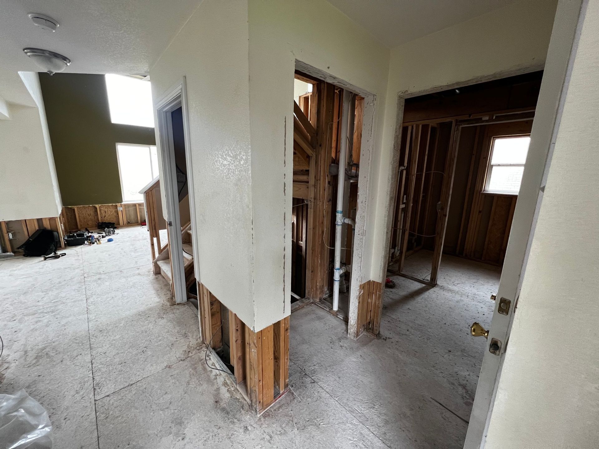 Interior view of a residential construction site featuring partially demolished walls, exposed wood studs, and subflooring.