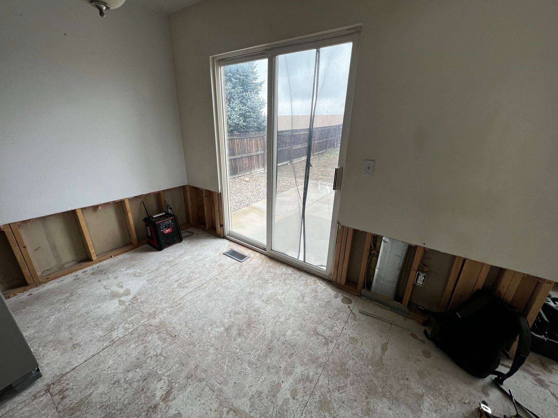 An interior room under renovation with removed drywall, exposing wall studs, and sliding glass doors leading to a patio.