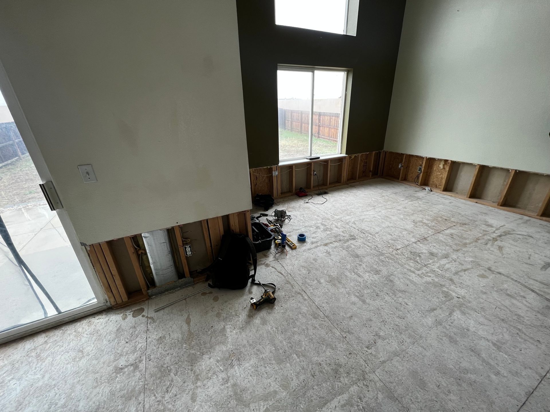 An interior room under construction with exposed wall studs, subflooring, a sliding door, and windows.