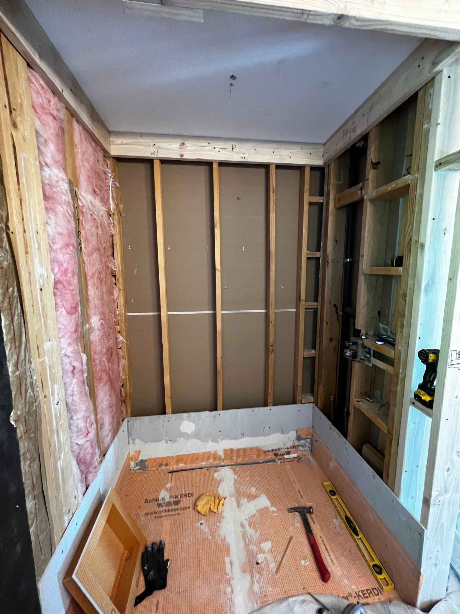 A construction site of a bathroom shower stall with wood framing, wall insulation, and orange waterproof floor membrane.