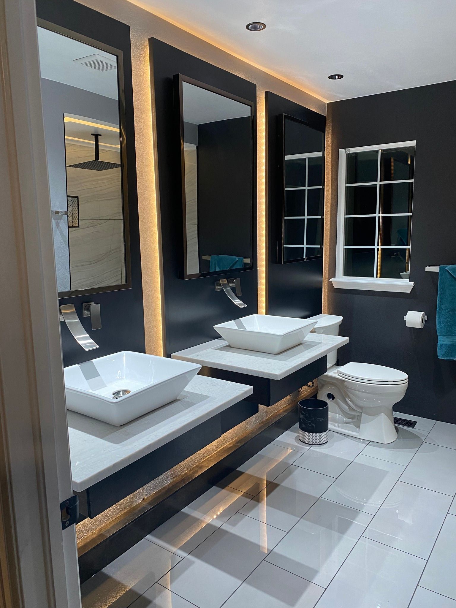 A modern kitchen with light grey wooden cabinets, stainless steel appliances, white countertops, and herringbone tile.