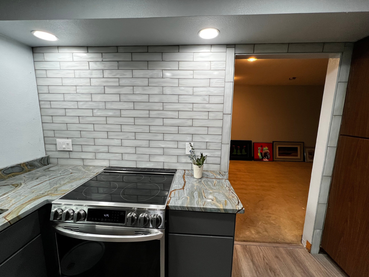 A kitchen counter with a gray brick backsplash, stainless steel oven, and granite countertop beside a doorway.