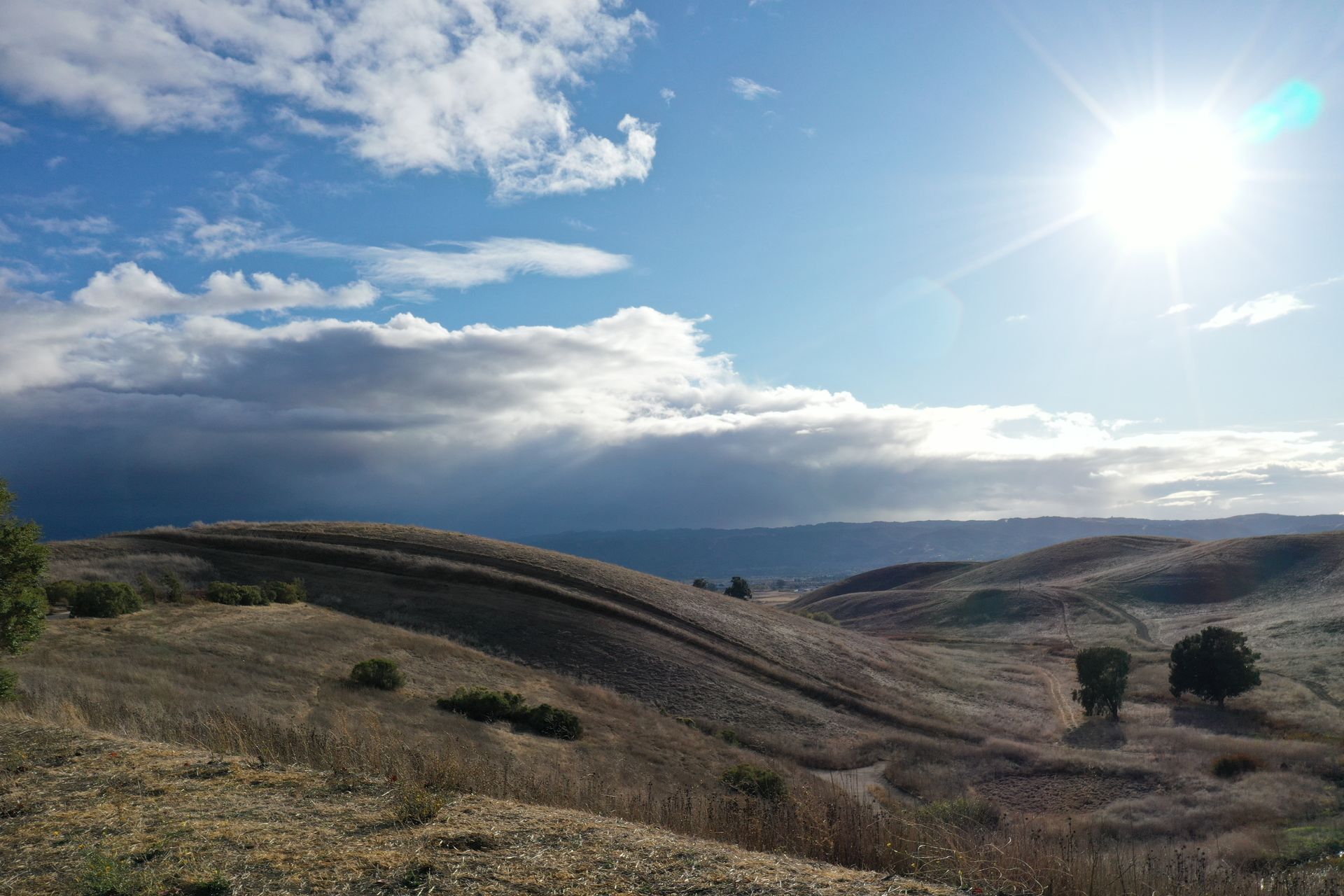 The sun is shining through the clouds over a desert landscape.