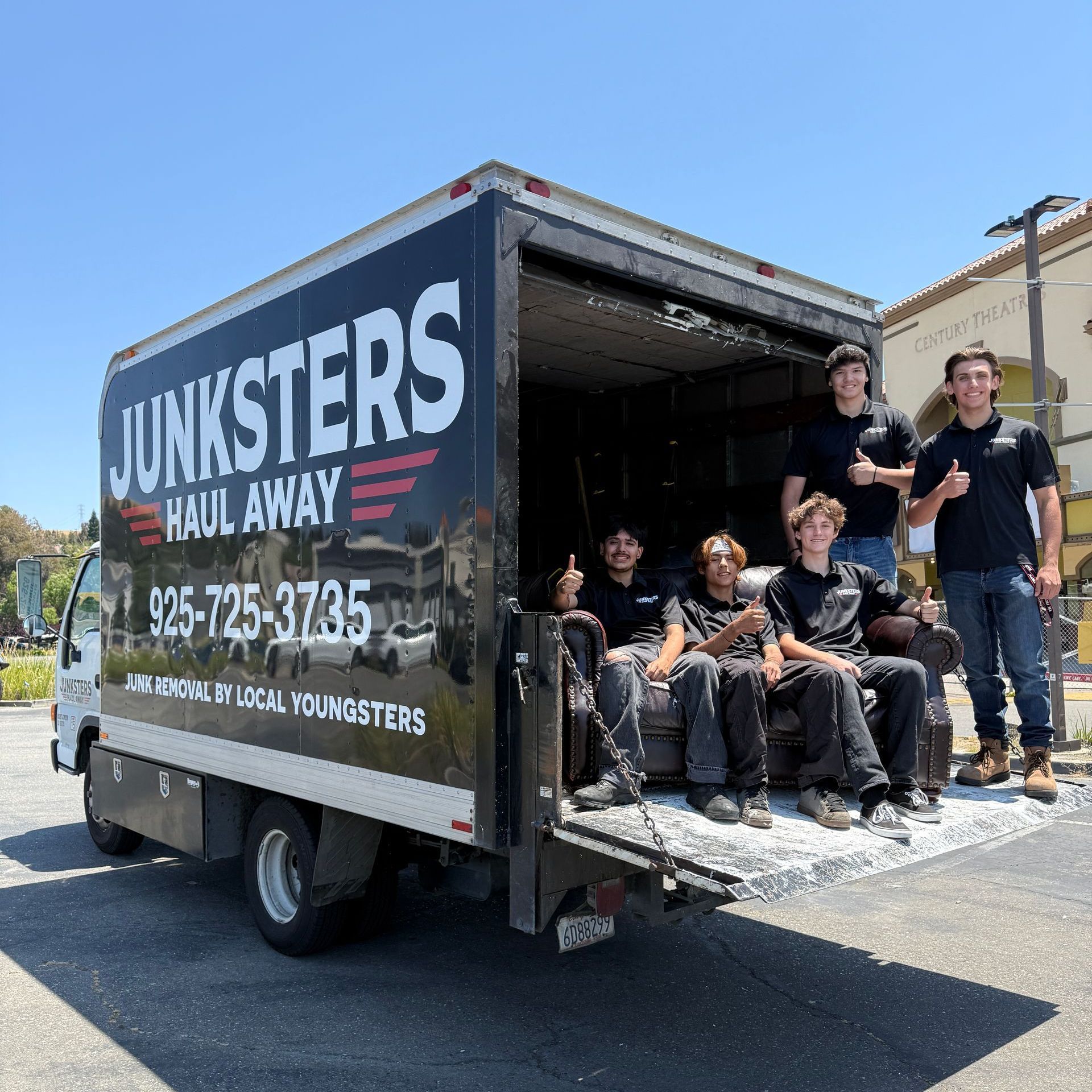 Three men are posing for a picture in front of a truck full of junk.