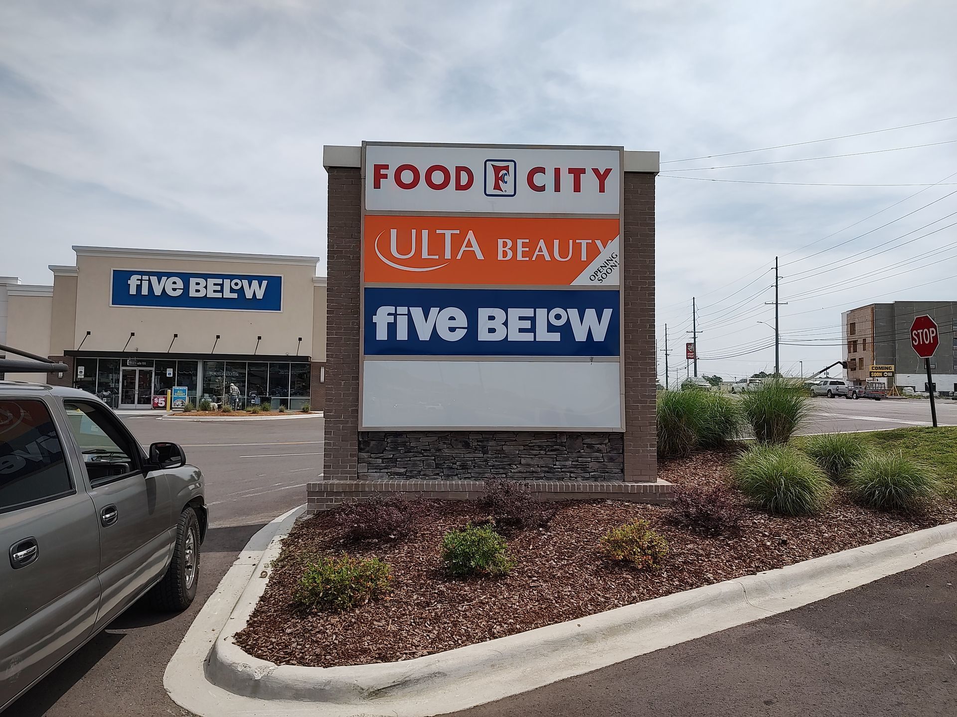 A car is parked in front of a sign for food city and five below.