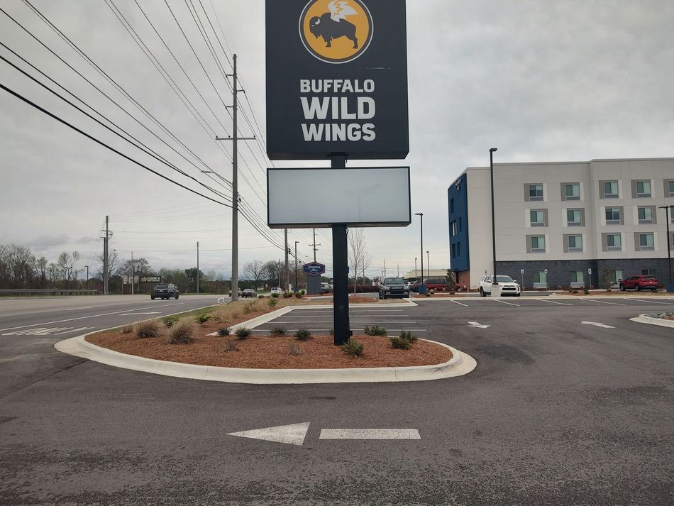 Buffalo Wild Wings sign at a roadside, arrow points left. A hotel is in the background. Overcast sky.