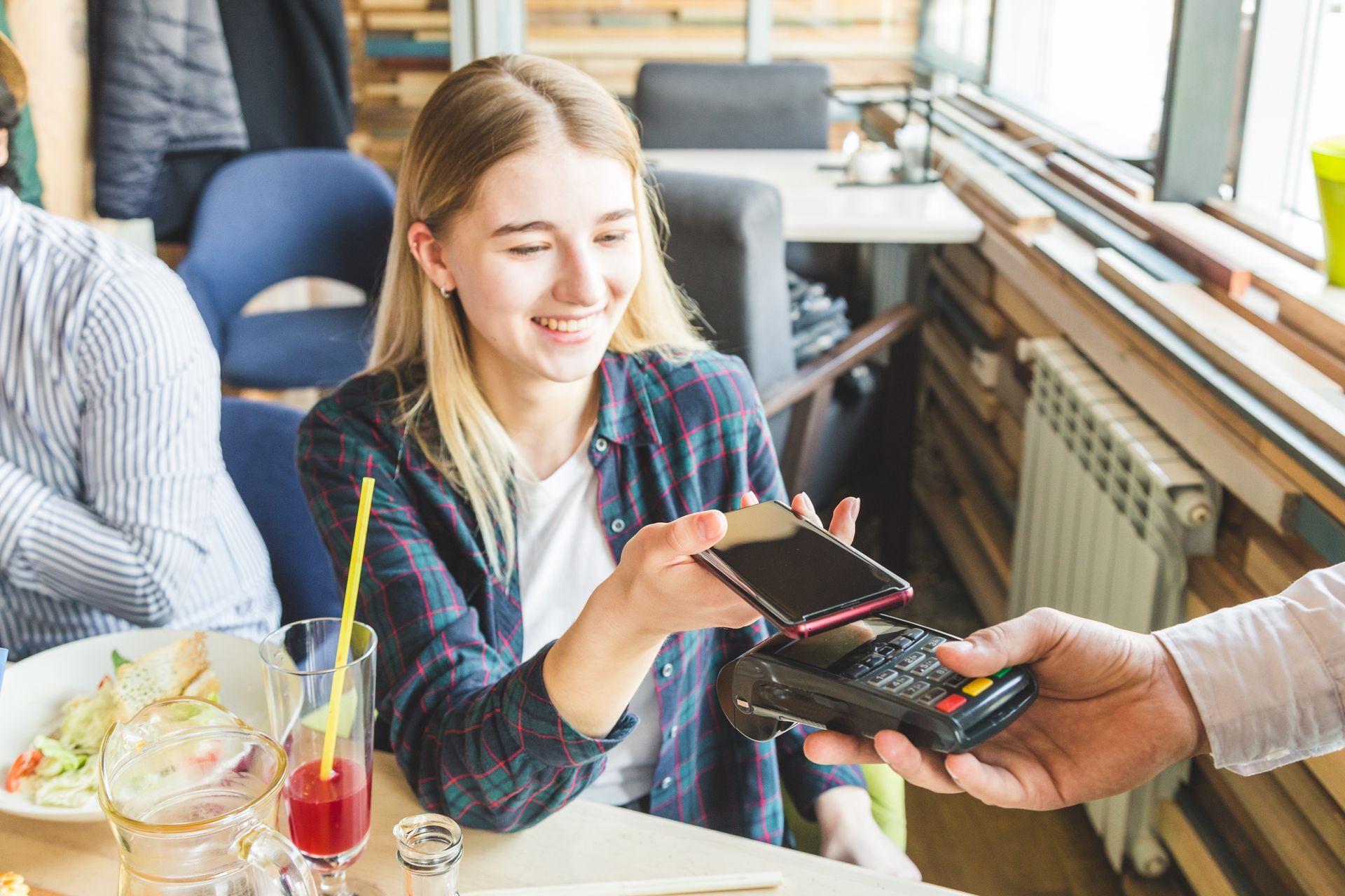 A smiling woman paying in a restaurant with a contactless smartphone payment. A smiling woman paying in a restaurant with a contactless smartphone payment.