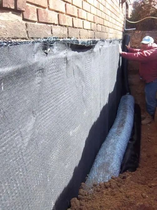 A person is standing in front of a brick wall.