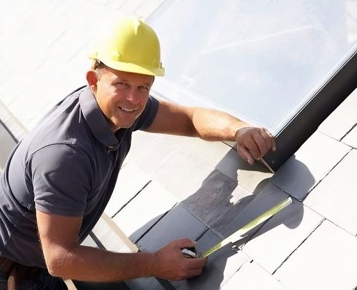 A Man Wearing A Hard Hat Is Measuring A Roof Wth A Tape Measure
