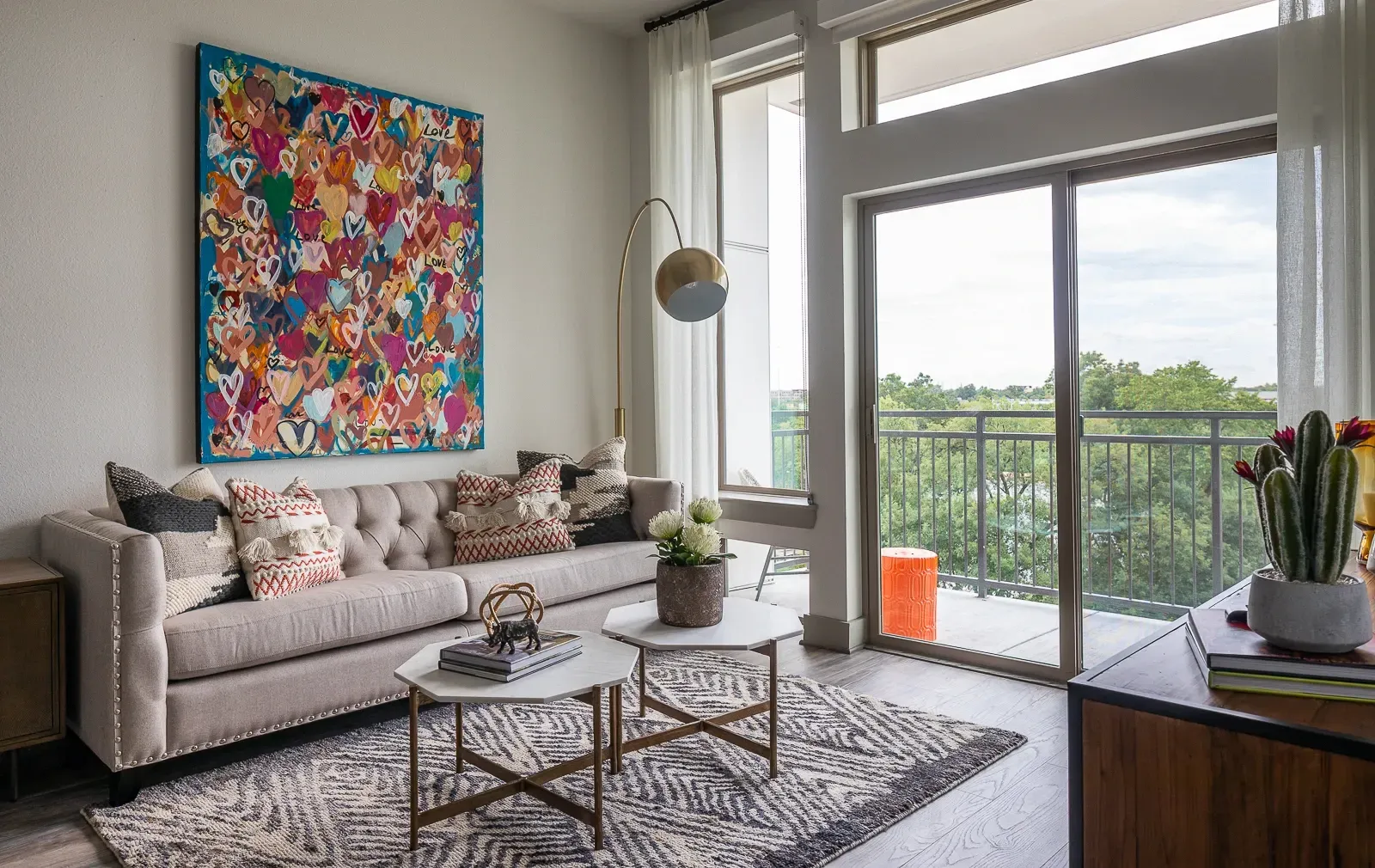Stylish living room with tufted sofa, patterned rug, large abstract art, and balcony access.