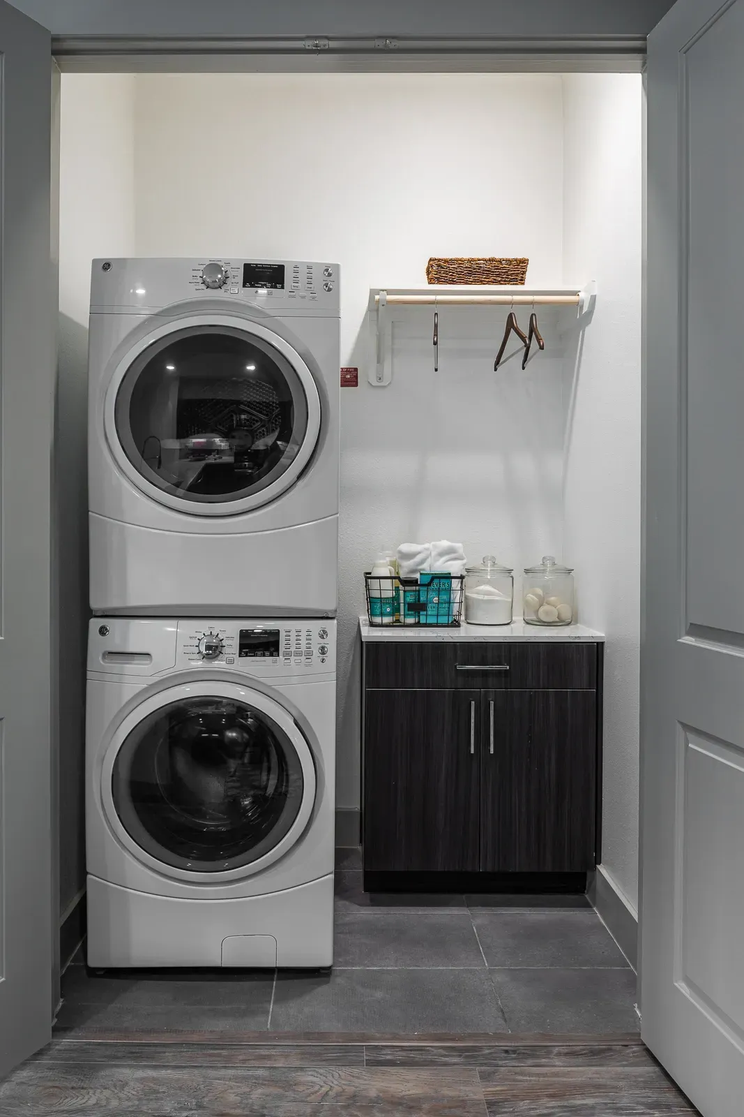 Stackable washer and dryer unit with a small cabinet and shelf above.