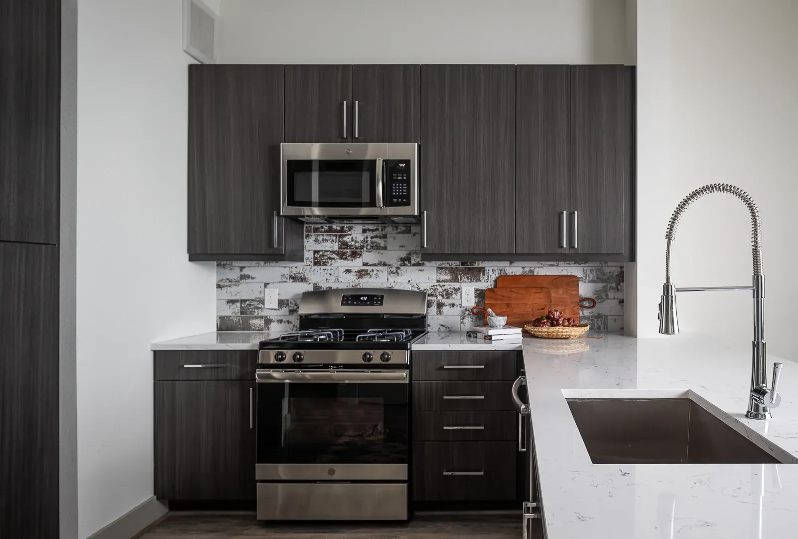 Modern kitchen with dark gray cabinets, stainless steel appliances, and a large sink.