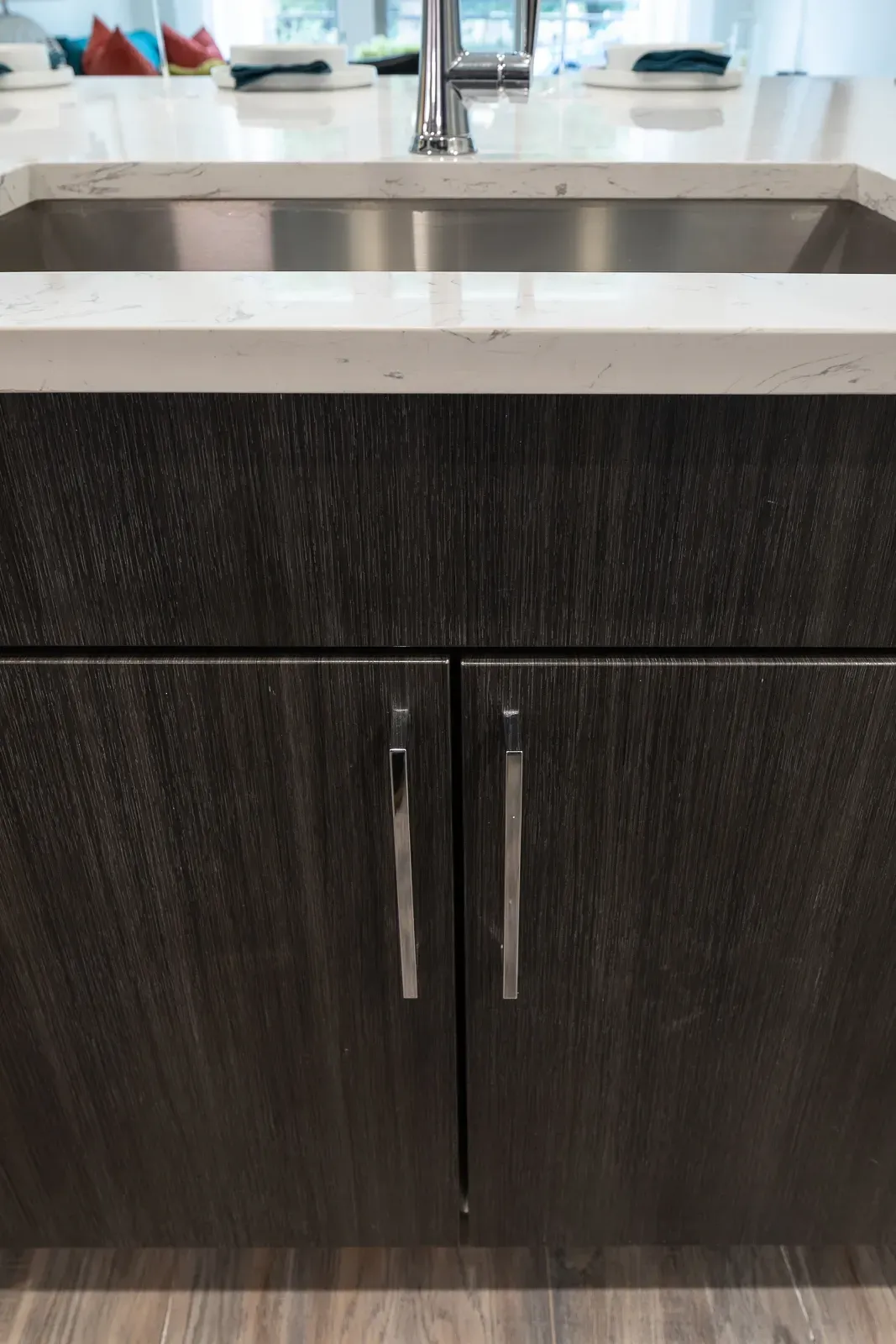 Close-up of a modern kitchen island with a stainless steel sink and dark wood cabinetry.