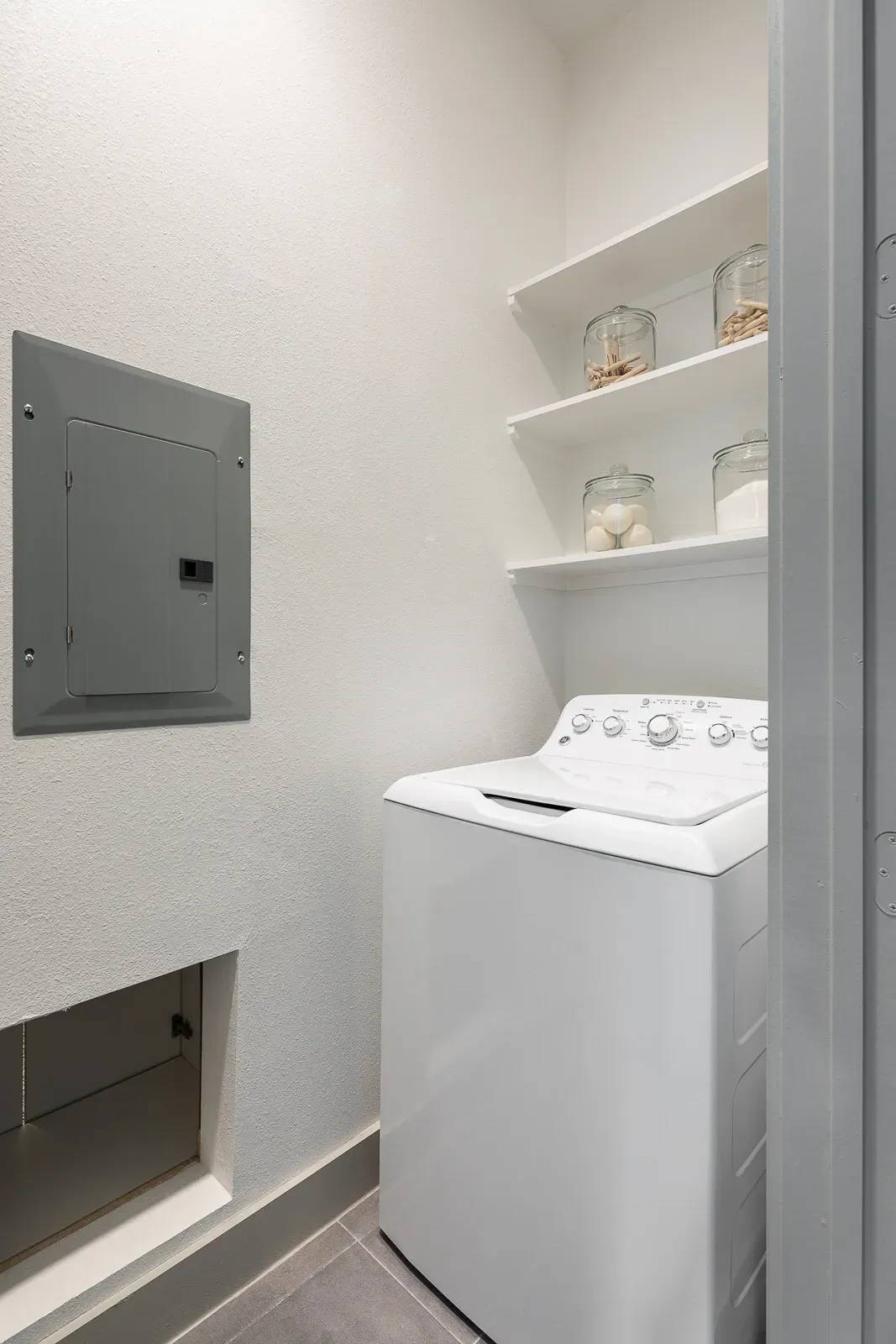 In-unit washer and dryer with storage shelves and an electrical panel.